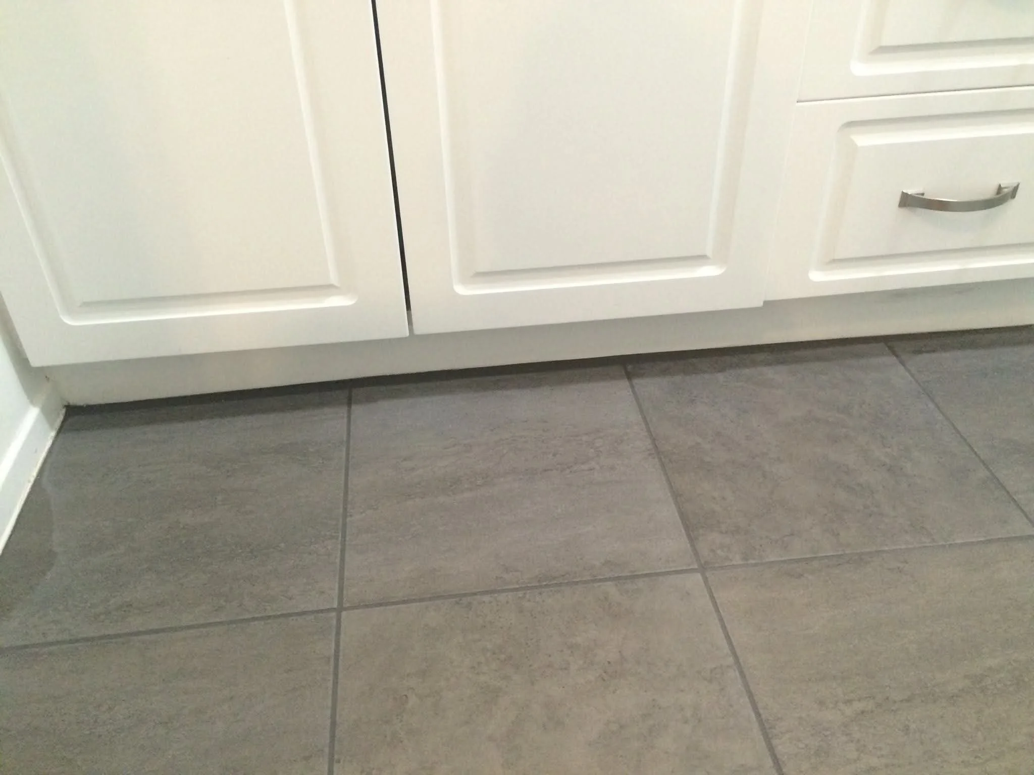 Close-up of the bottom of white kitchen cabinets and gray tiled floor.