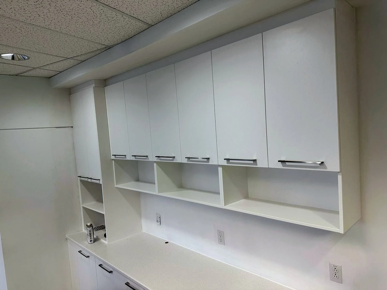 Empty white kitchen cabinets with black handles, open shelves, and a white countertop.