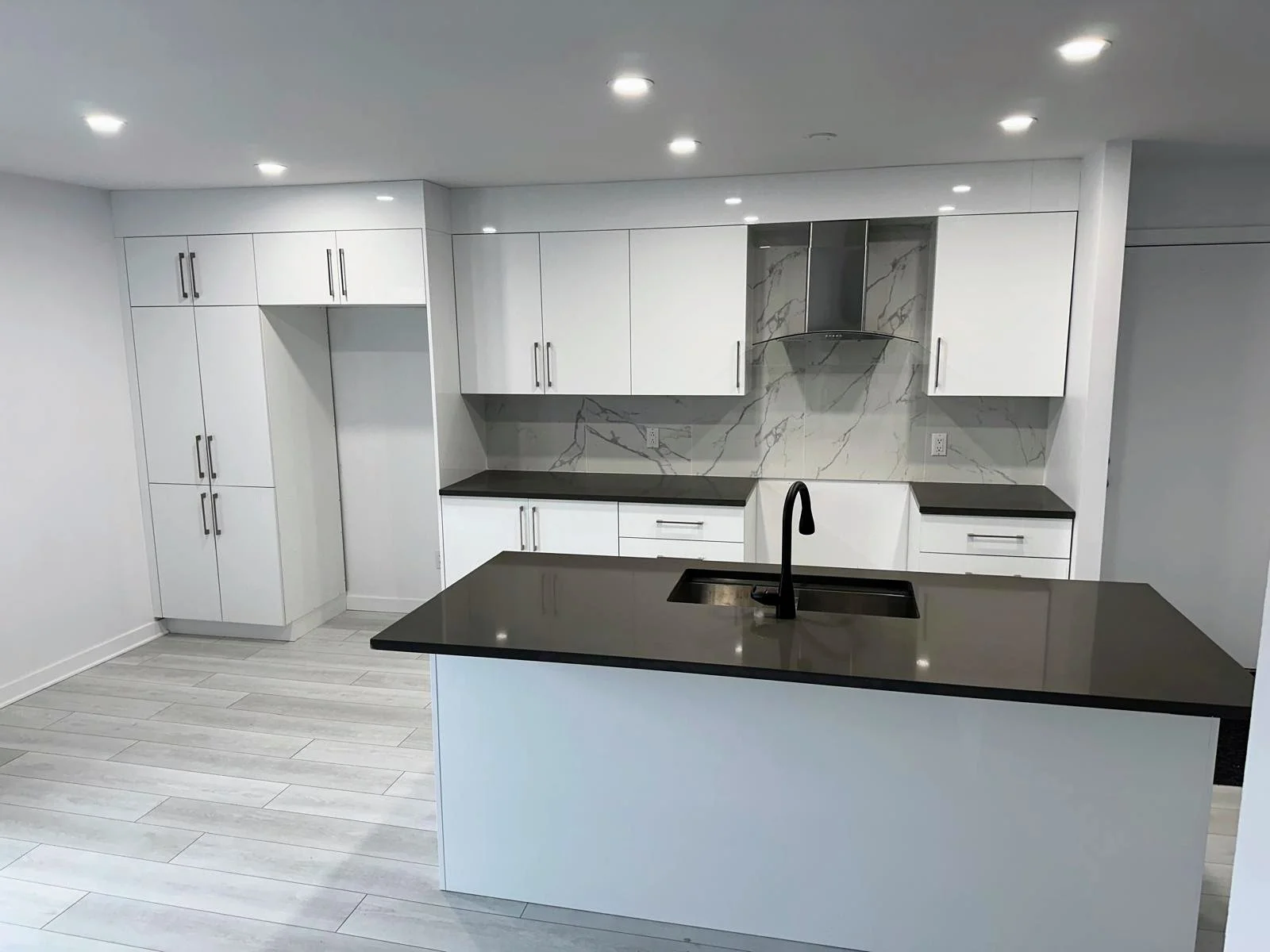 Modern kitchen with white cabinets, black countertops, a black sink, and a marble backsplash.