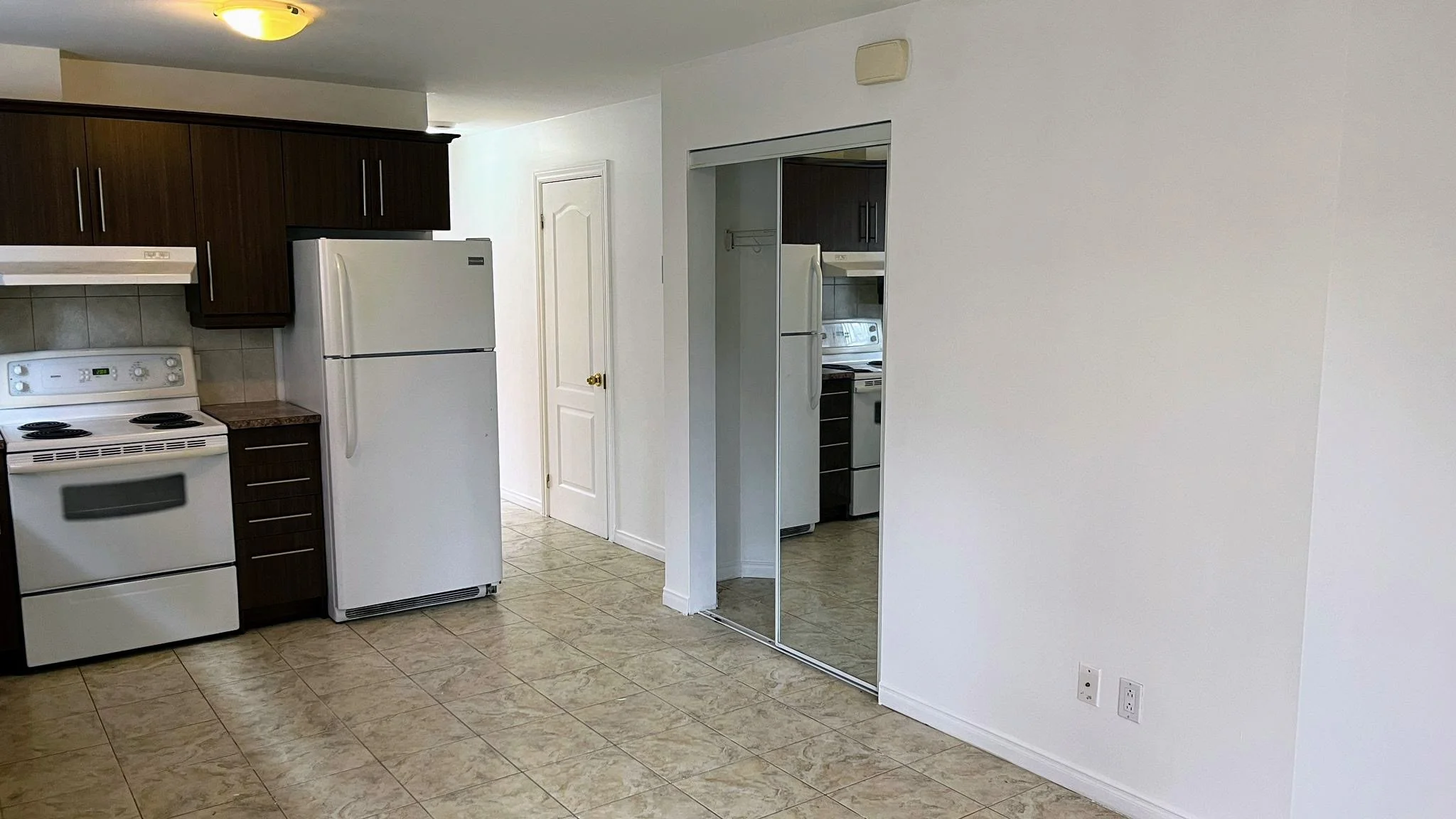 Kitchen with white appliances, dark wood cabinets, tile floor, and a mirrored sliding closet door.