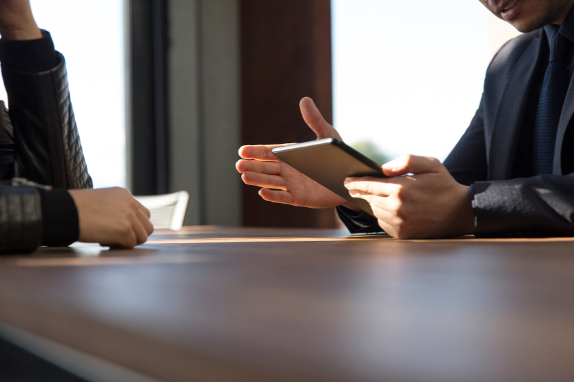 Businesspeople having a discussion at a table, with one person showing something on a tablet device.