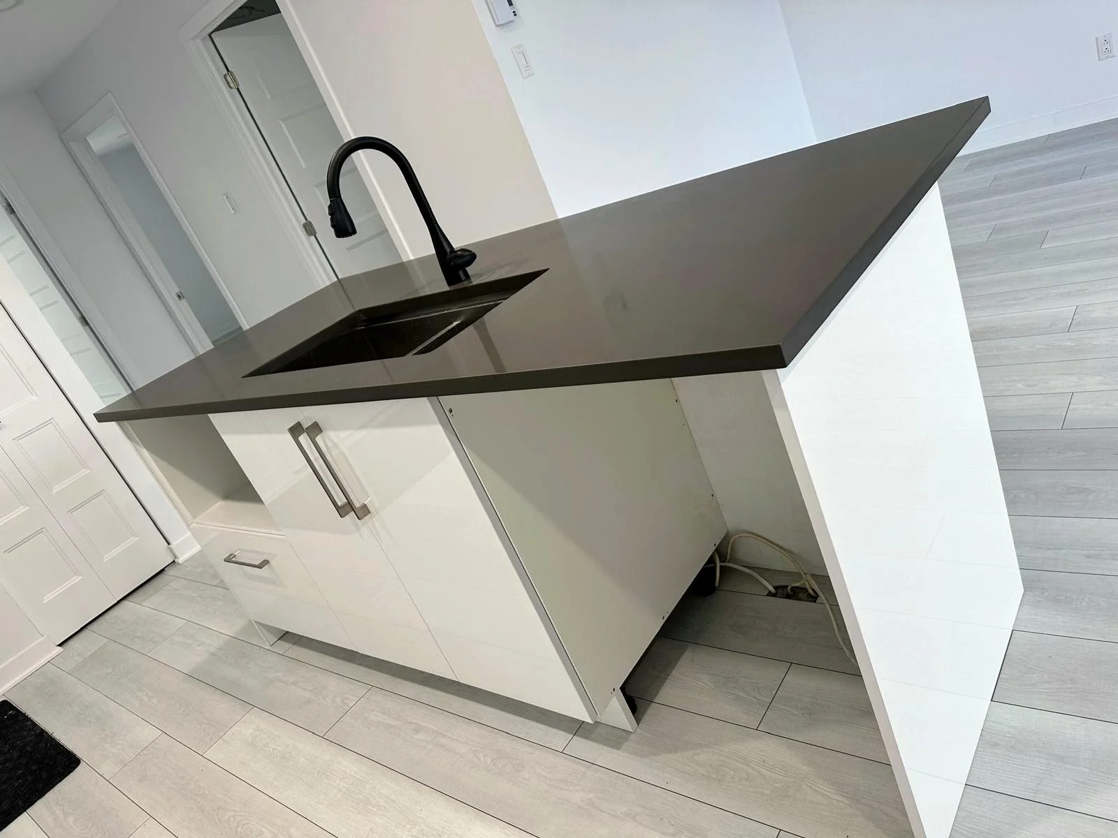 Modern kitchen island with a black countertop, sink, and faucet, white base cabinets, and light wood flooring.