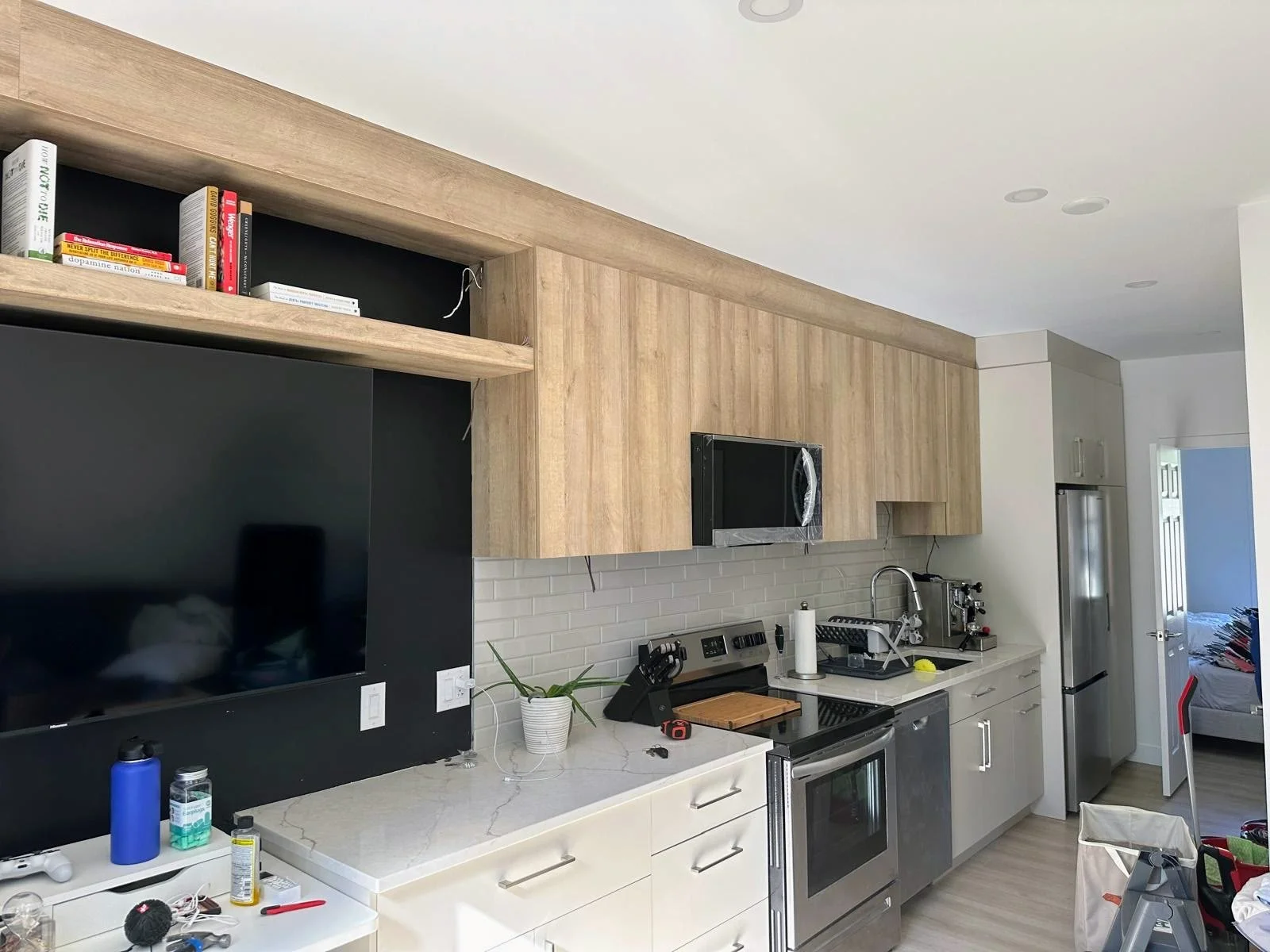 Kitchen with wooden cabinetry, stainless steel appliances, a microwave, and various items on the countertop including a plant, paper towel roll, and kitchen tools.