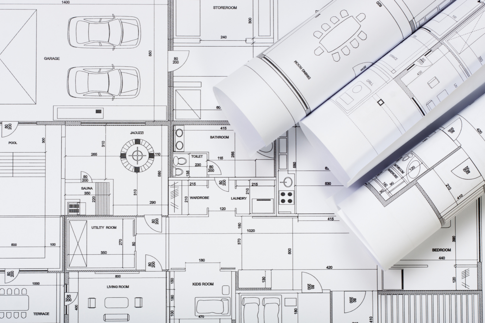 Architectural plans of a house layout with rooms labeled, drawings of a garage, pool, and various interior spaces on blueprints, with some pages rolled up.