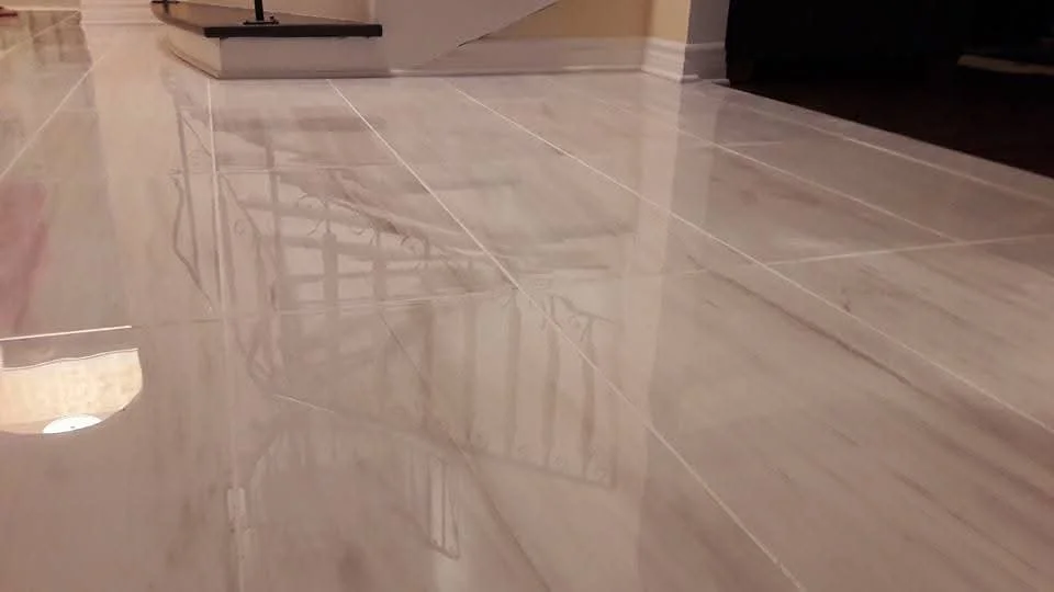 Close-up of a shiny marble tile floor in a home interior with reflections of a staircase and railing.