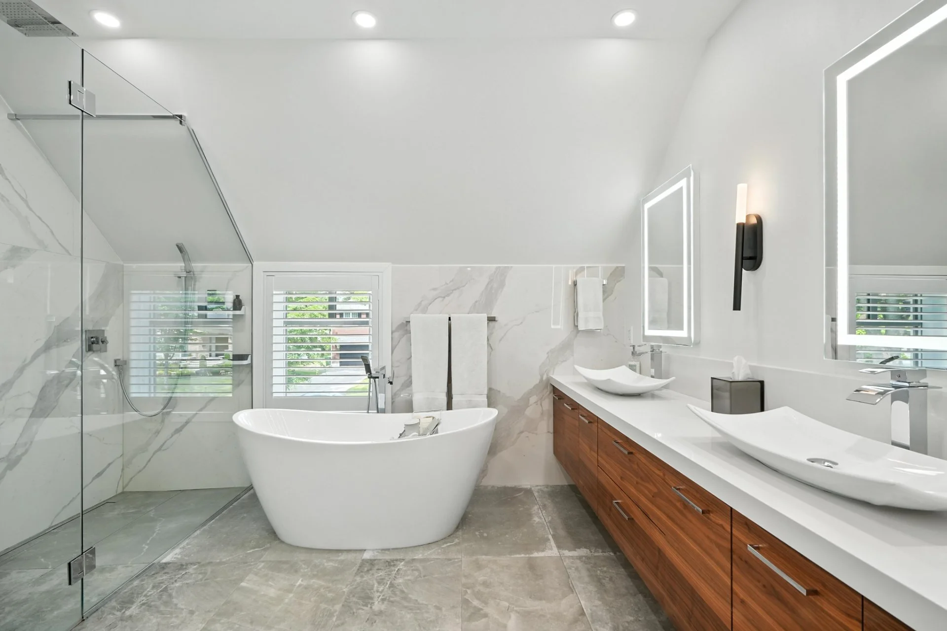 Modern bathroom with white walls, a freestanding bathtub, a double vanity with vessel sinks, and a walk-in shower enclosed with glass.