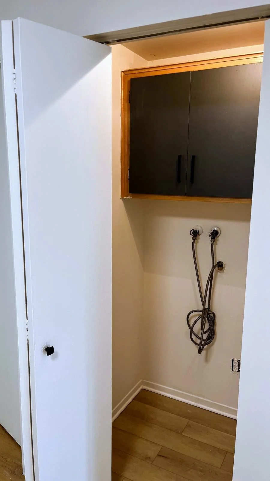 Empty laundry closet with black cabinets, connected water hoses, and a space for a washer and dryer.
