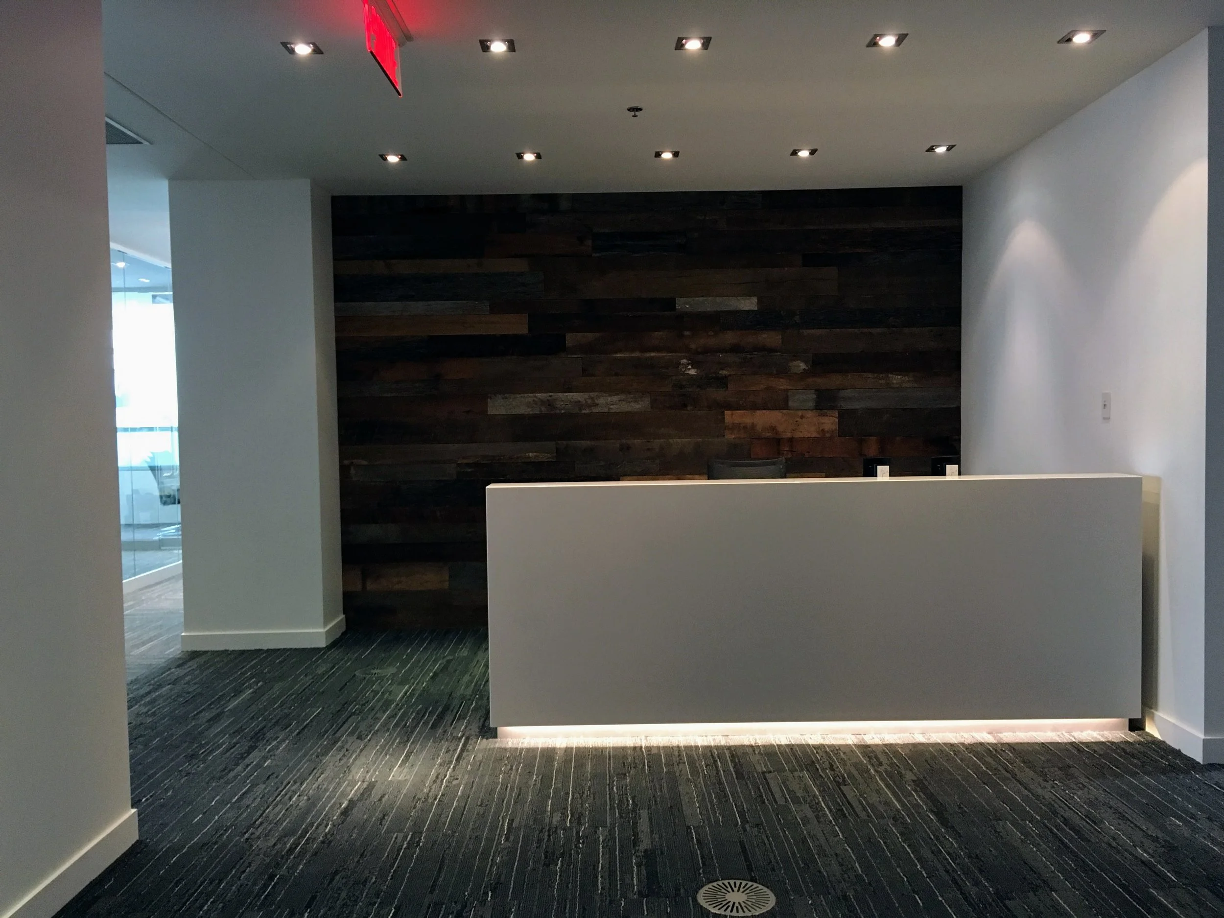Empty modern reception desk in an office with a dark wooden accent wall and carpeted floor.