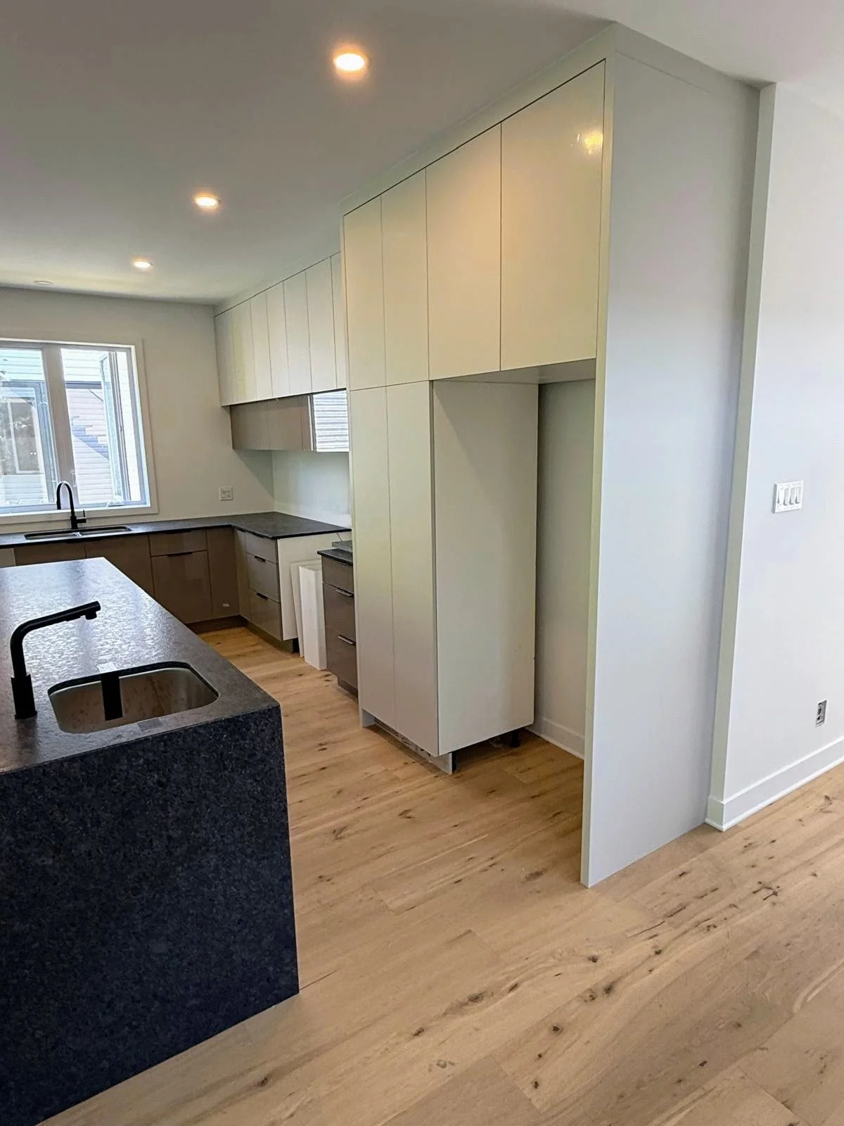 Modern kitchen with white and gray cabinetry, wooden flooring, and a black countertop island.
