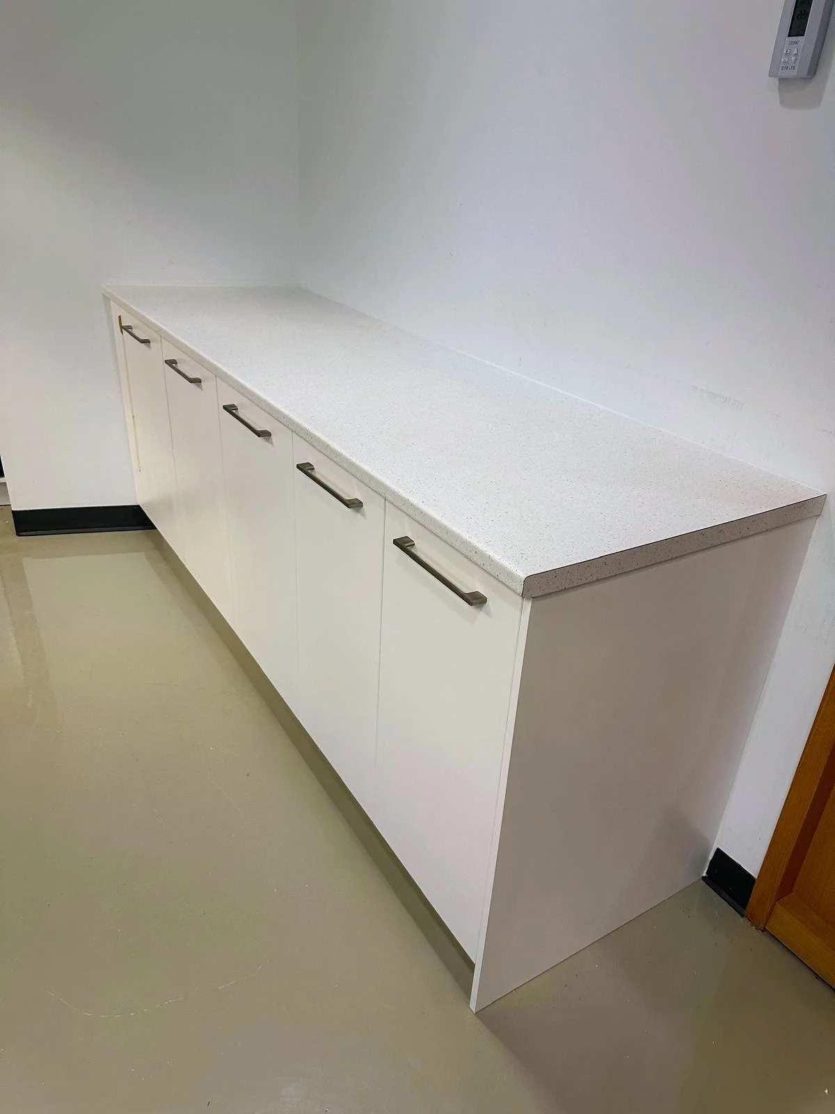 A white countertop with five cabinet drawers underneath, located against a white wall in a room.