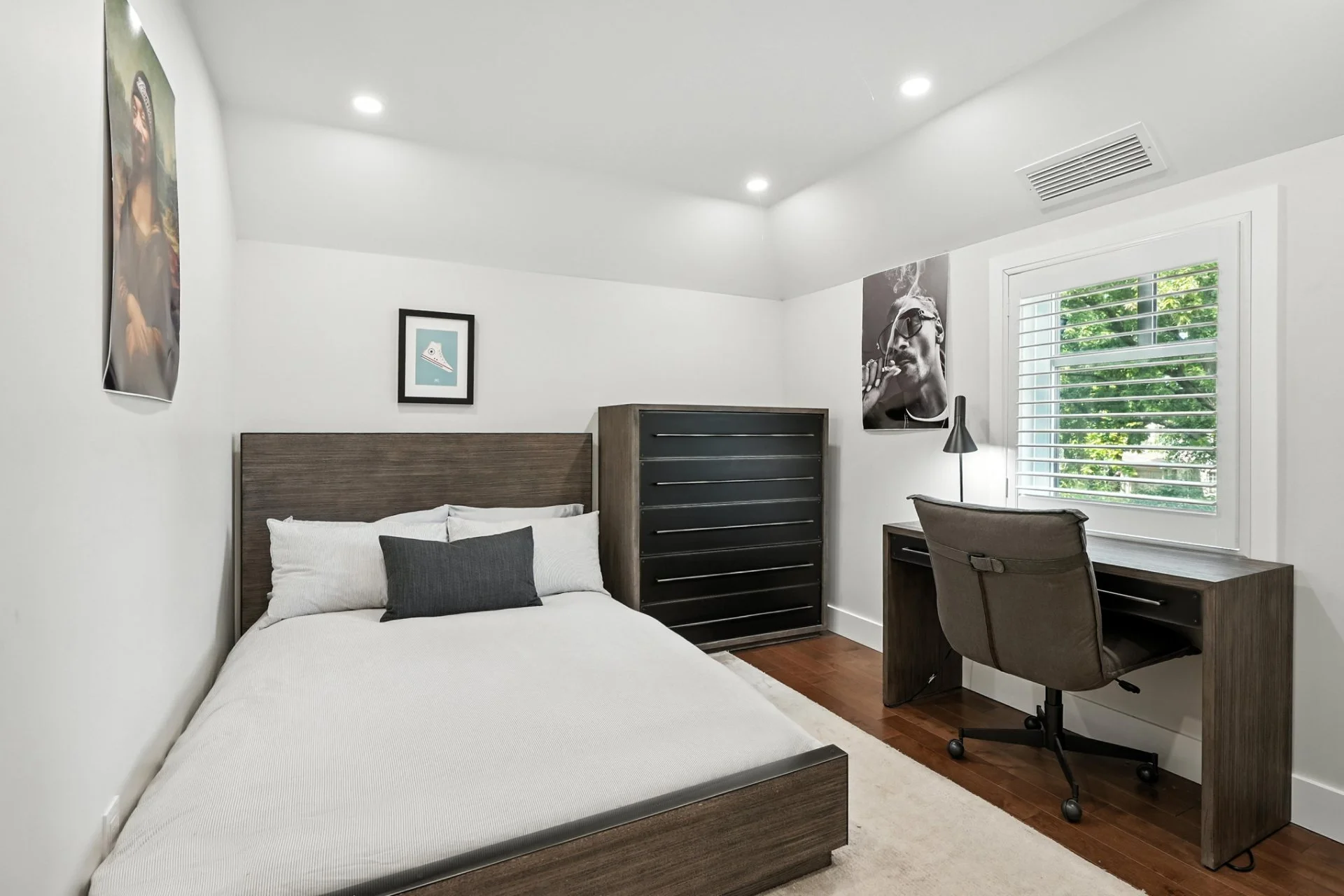 Bedroom with a bed, black dresser, desk, chair, window with blinds, and wall art