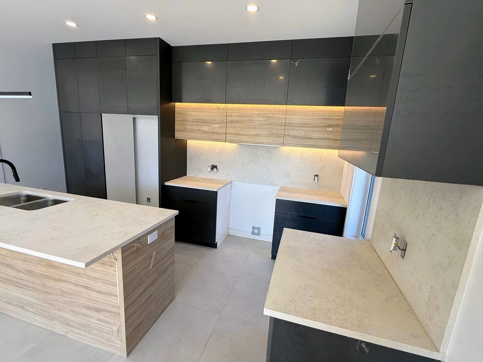 Modern kitchen with black and wood cabinetry, light-colored countertops, and under-cabinet lighting.