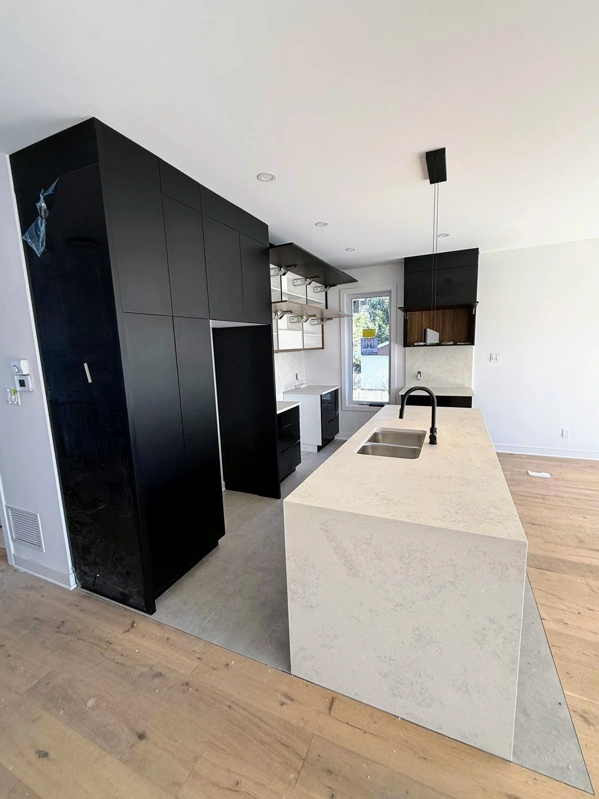 Modern kitchen with black cabinets, beige island with sink, wooden floors, and a window in the background.