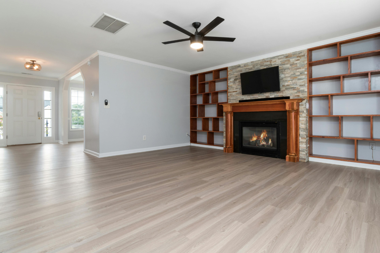 Empty living room with a fireplace, built-in shelves, a wall-mounted TV, and a ceiling fan.
