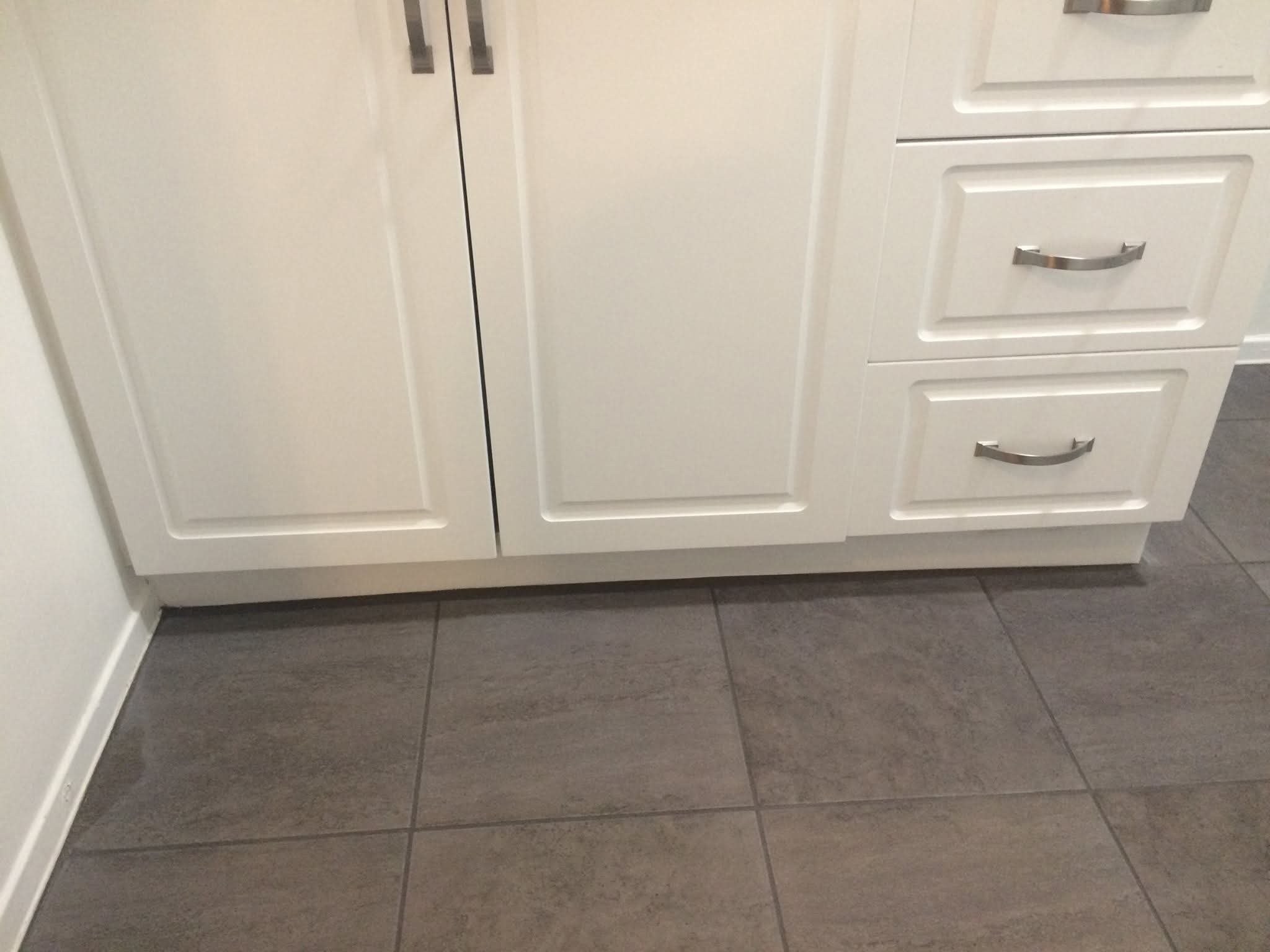 White kitchen cabinets with silver handles situated above tiled gray floor.