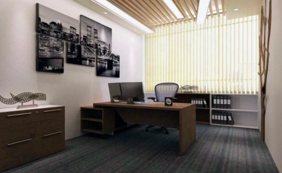 An office with a wooden desk, an office chair, a computer monitor, a side cabinet with decor, a framed cityscape photograph on the wall, and large windows with vertical blinds.