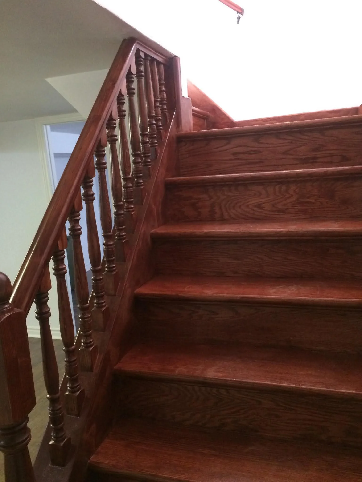 A wooden staircase with brown polished wood steps and matching wooden balustrade with turned spindles.
