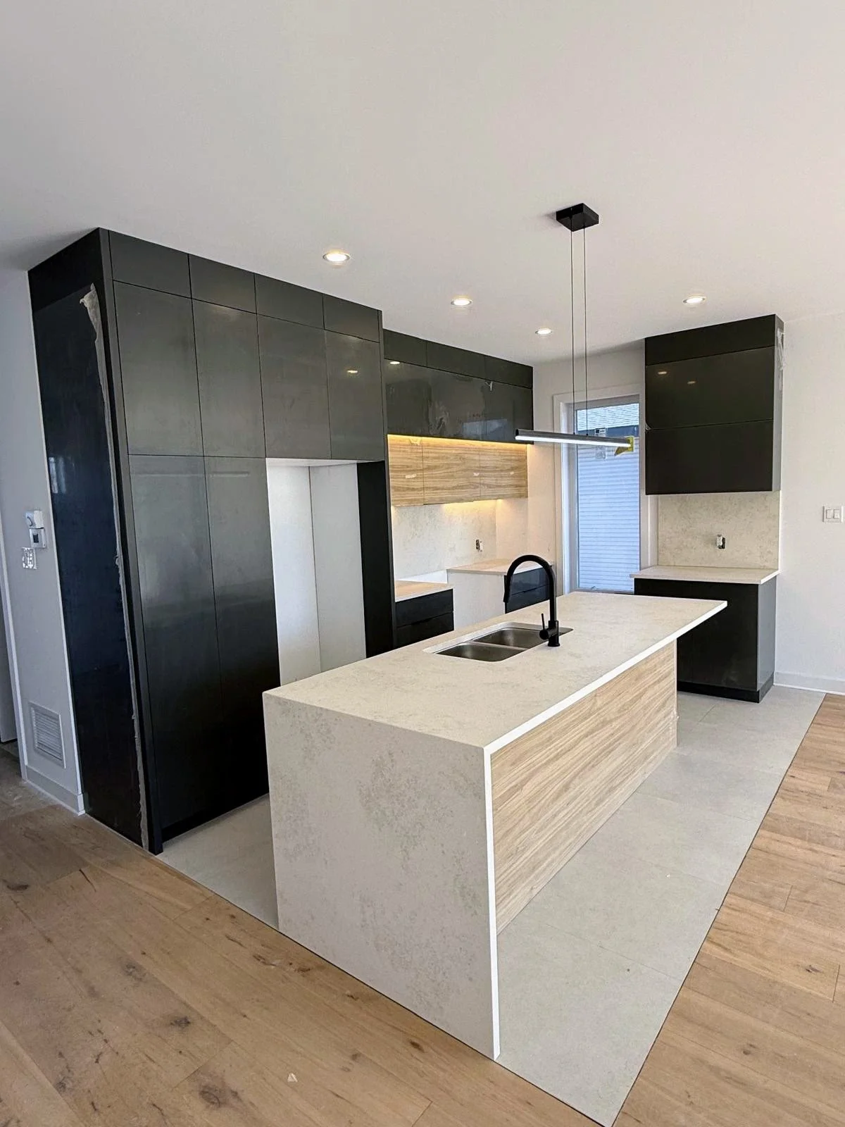 Modern kitchen with black cabinets, a white island with wood accents, black sink and faucet, and a suspended linear light fixture.