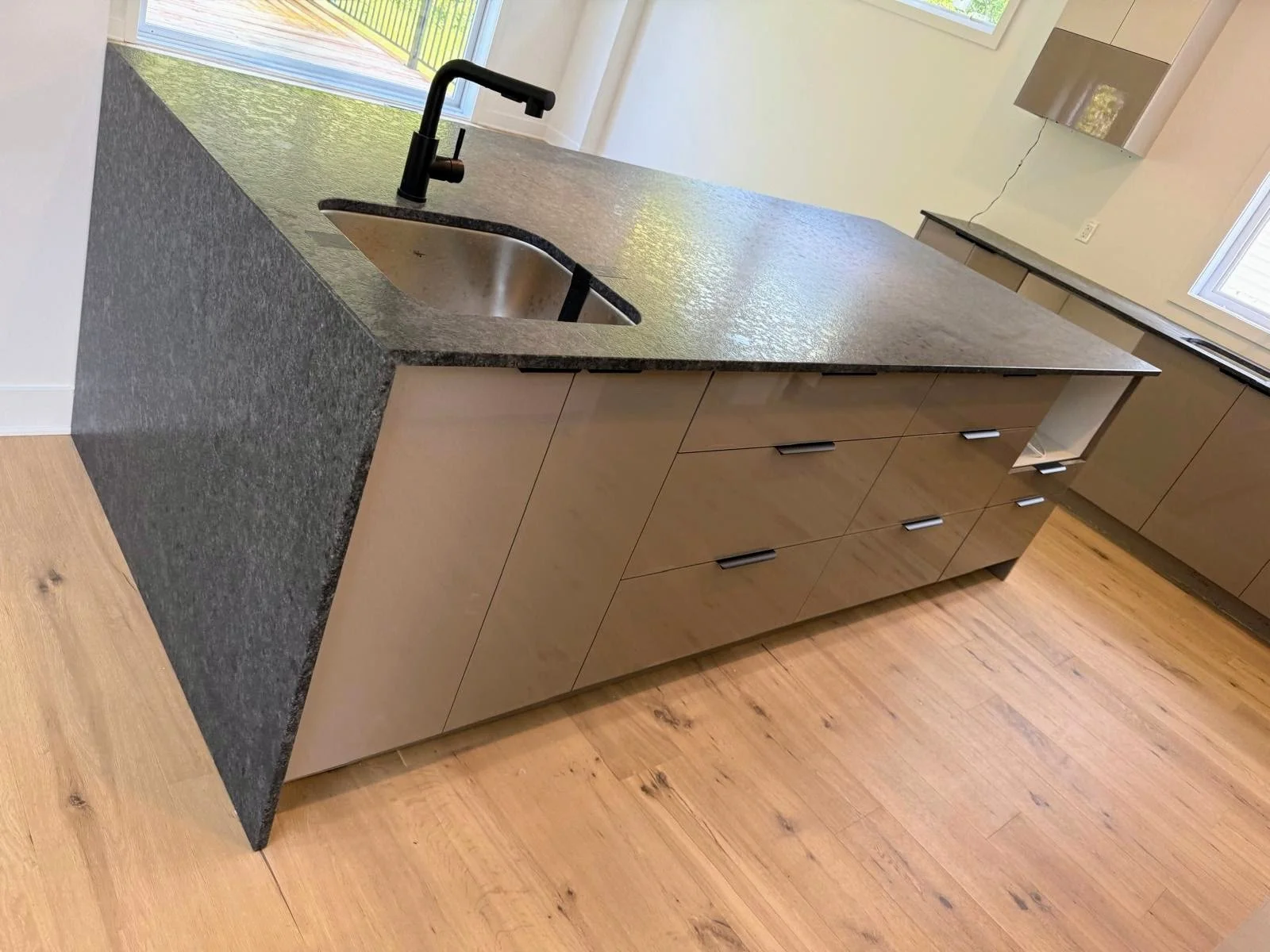 Modern kitchen island with black faucet and granite countertop, beige cabinets, and hardwood flooring.