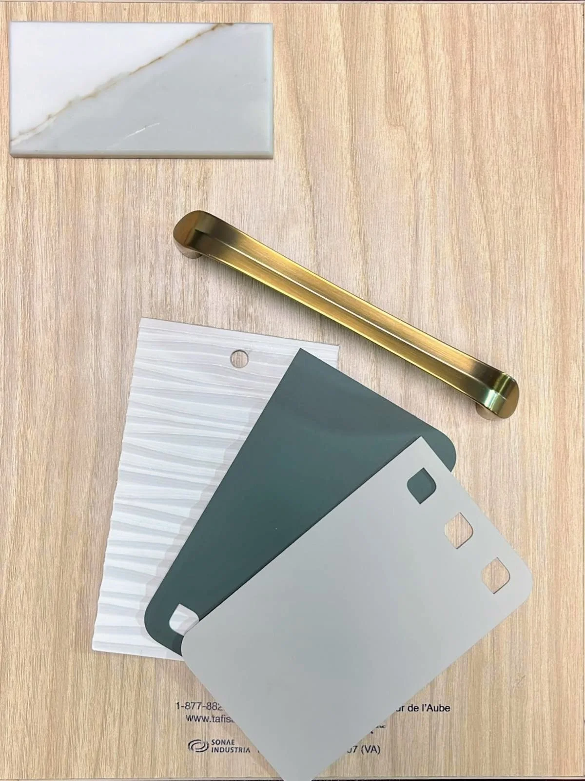 Samples of different wall paint color swatches, a brass paint scraper, and a piece of marble-like material on a wooden surface.