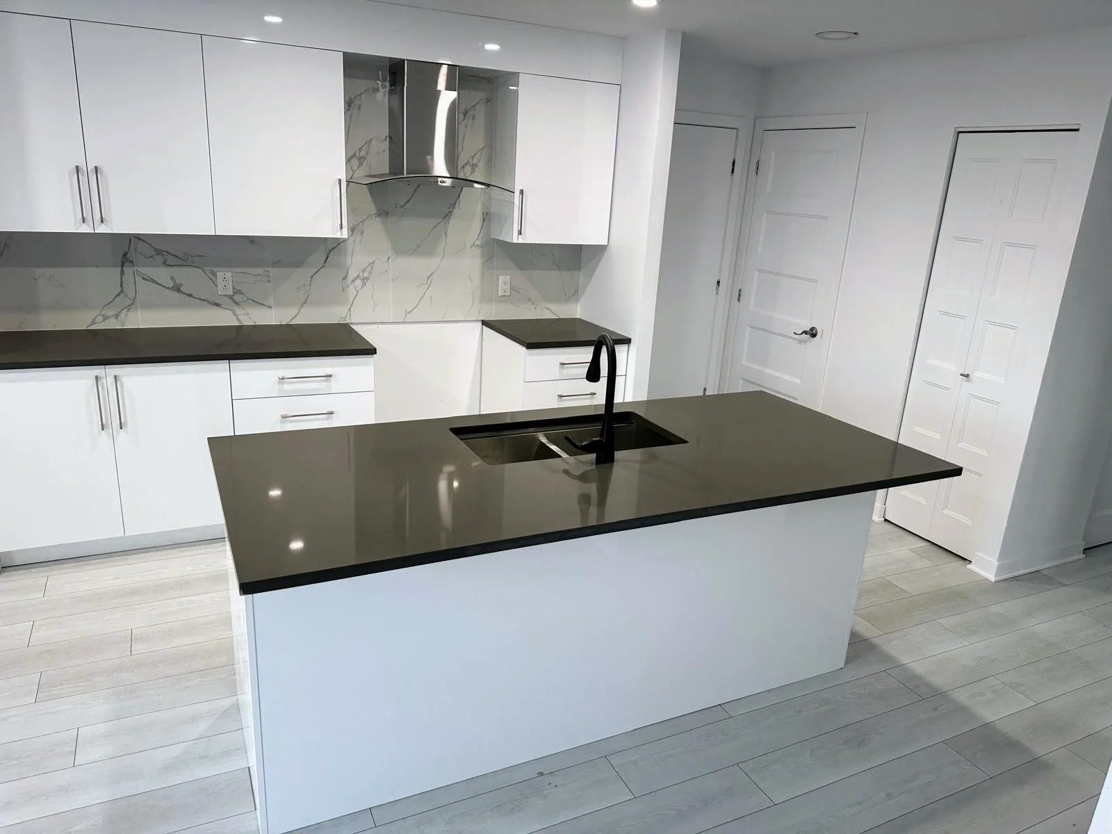Modern kitchen with white cabinets, black countertops, a black sink, and a marble backsplash, featuring an island with a sink.