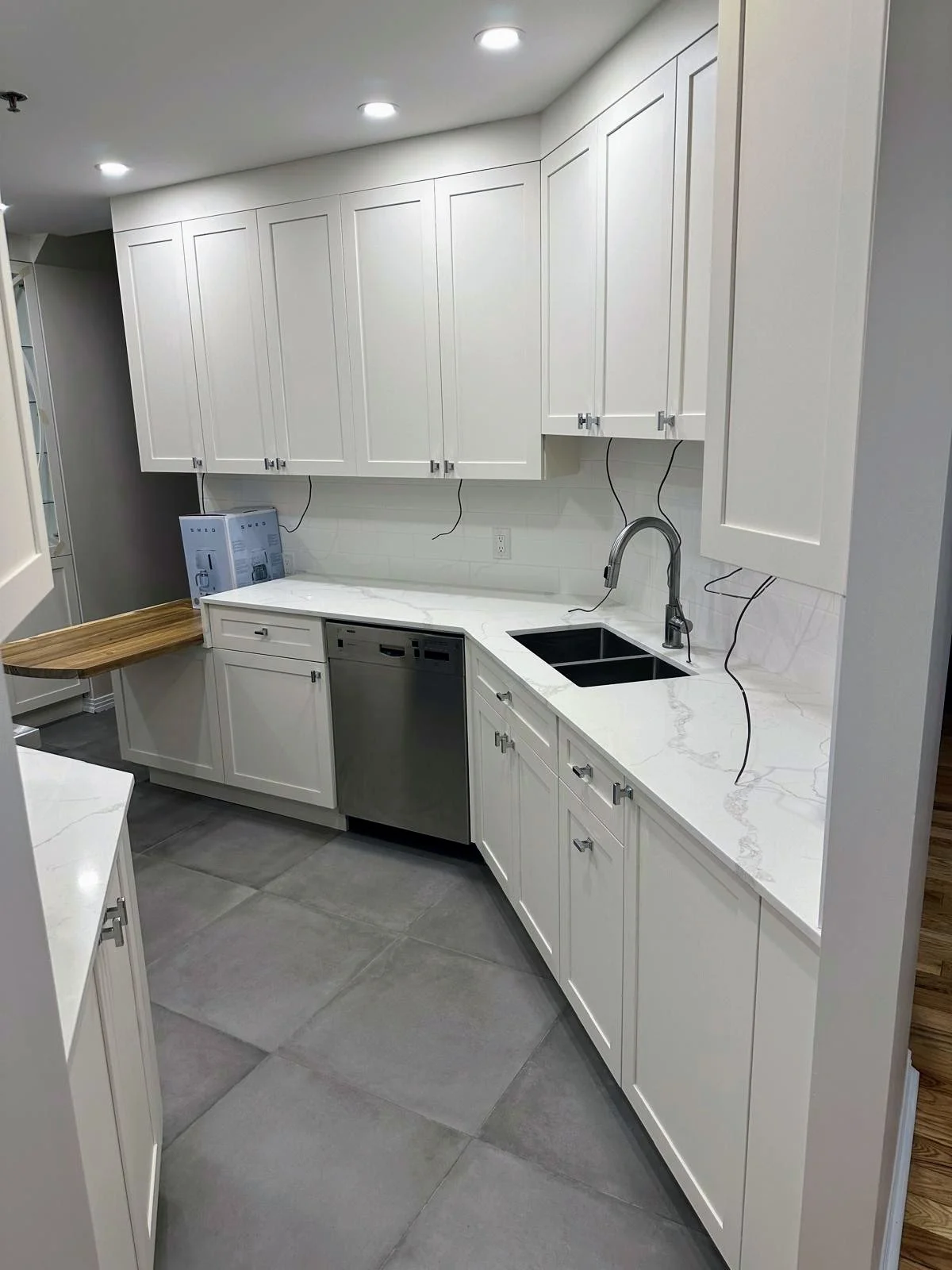 Kitchen with white cabinets, marble countertops, black undermount sink, silver faucet, gray tile flooring, and recessed ceiling lights.