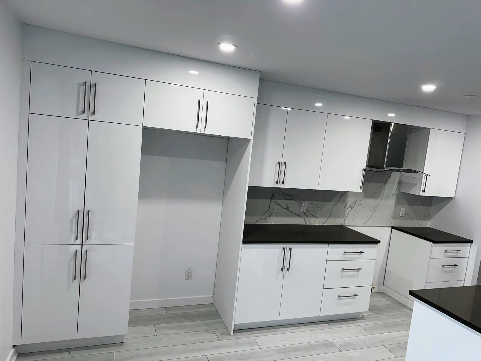 Modern kitchen with white cabinets, black countertops, and a marble backsplash, illuminated by ceiling lights.