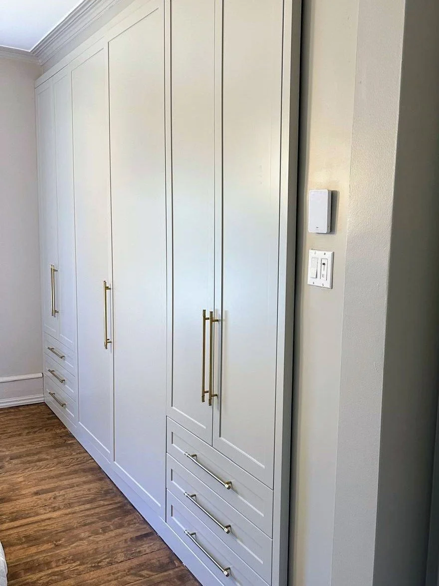 White built-in closet with gold handles and wooden floor in a room.