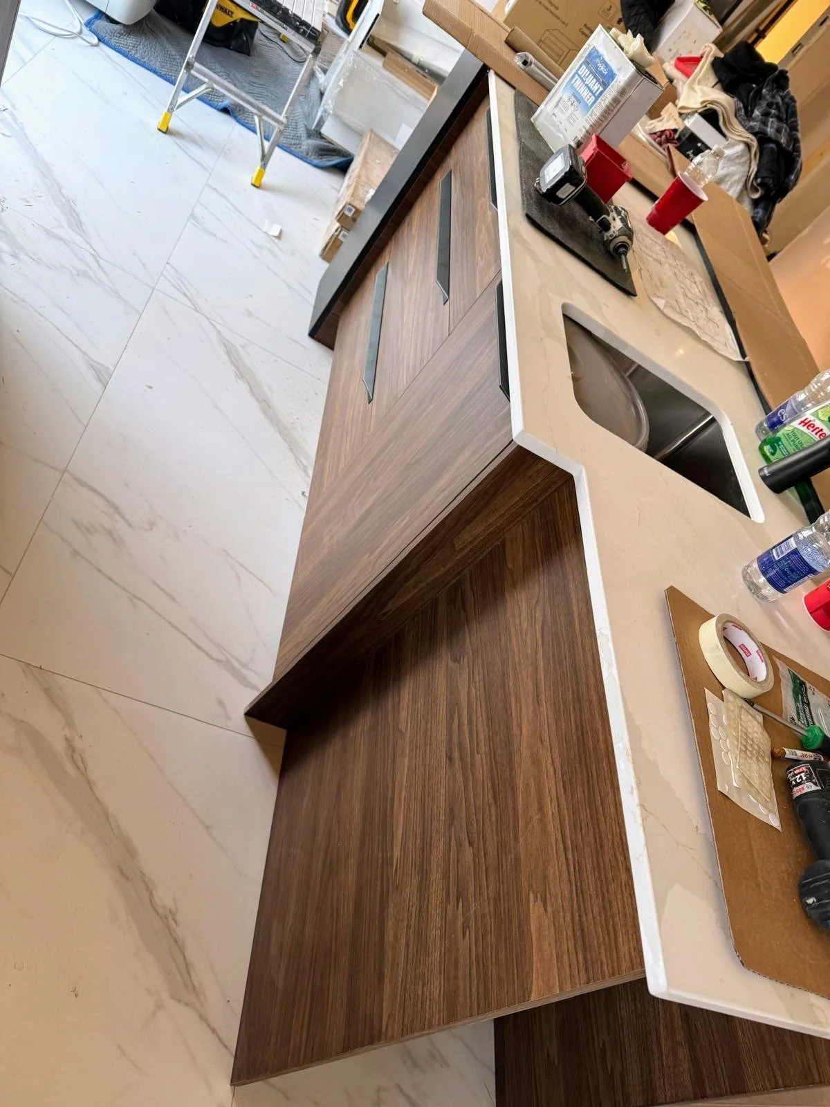 Kitchen island with a two-tone wood finish, white countertop, and various tools and supplies around it. In the background, there are construction materials and a ladder, indicating ongoing work.