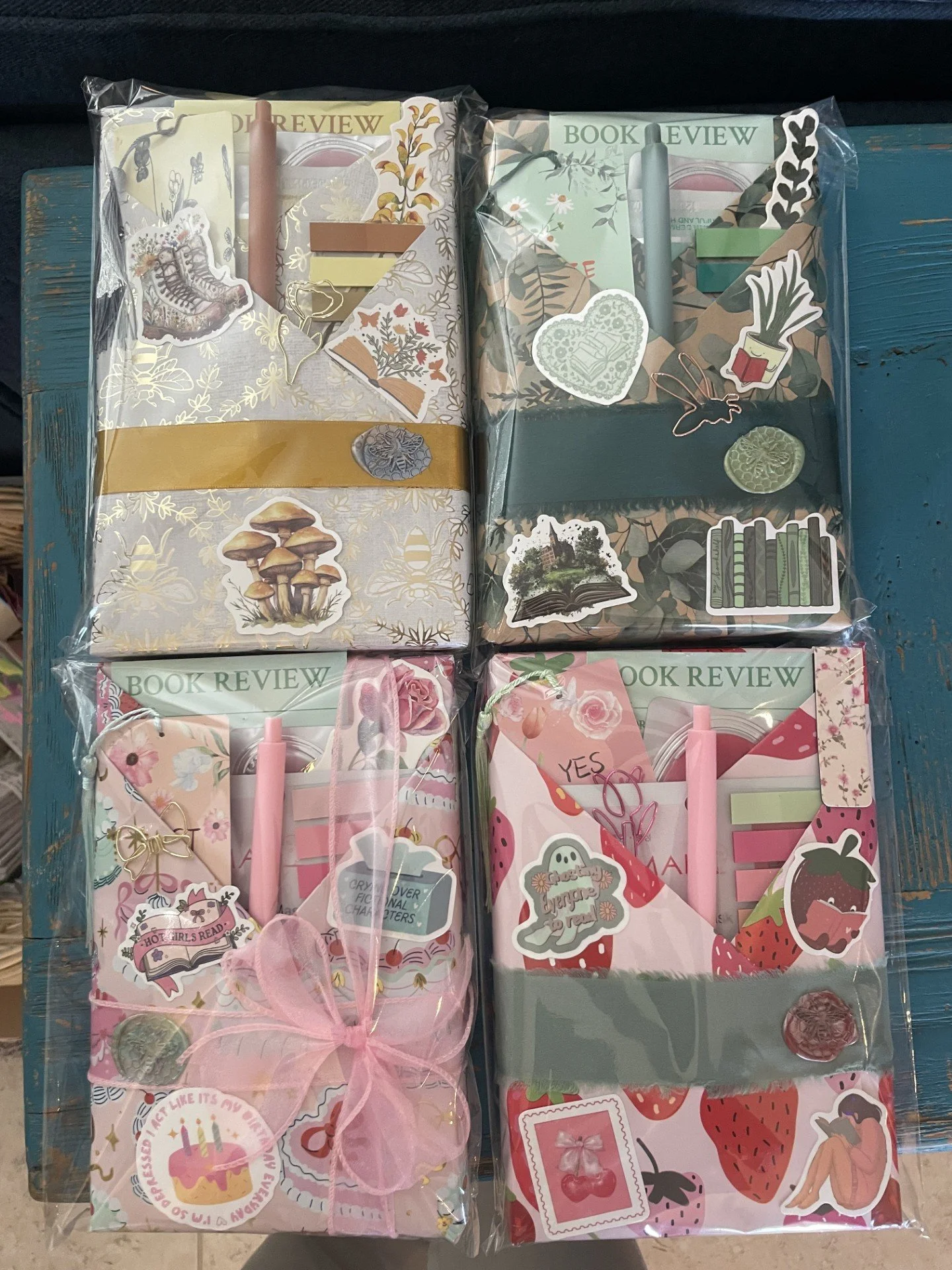 Four decorated notebooks with pens, stickers, and Post-it notes, each wrapped in clear plastic.