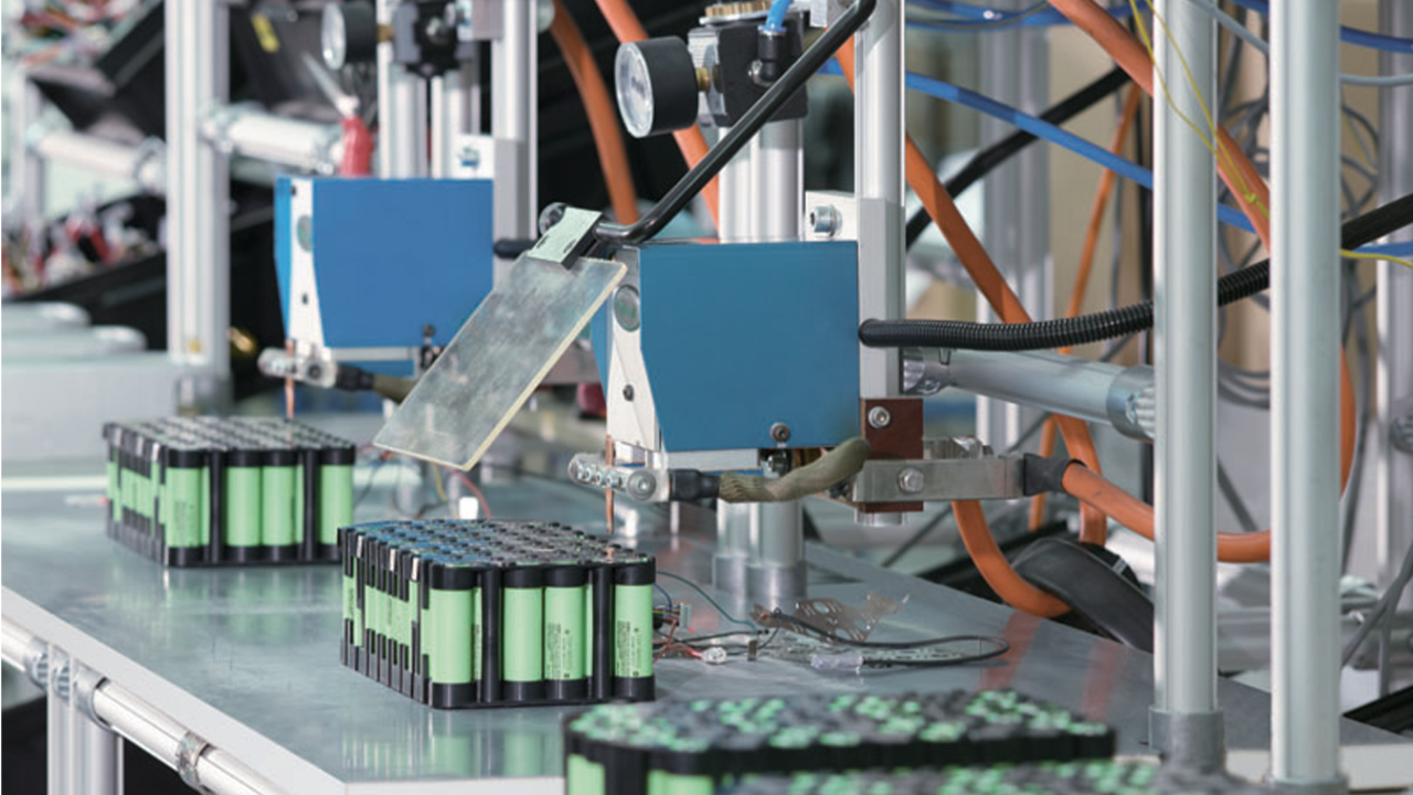 Industrial automation robots assembling and inspecting batteries on a production line.