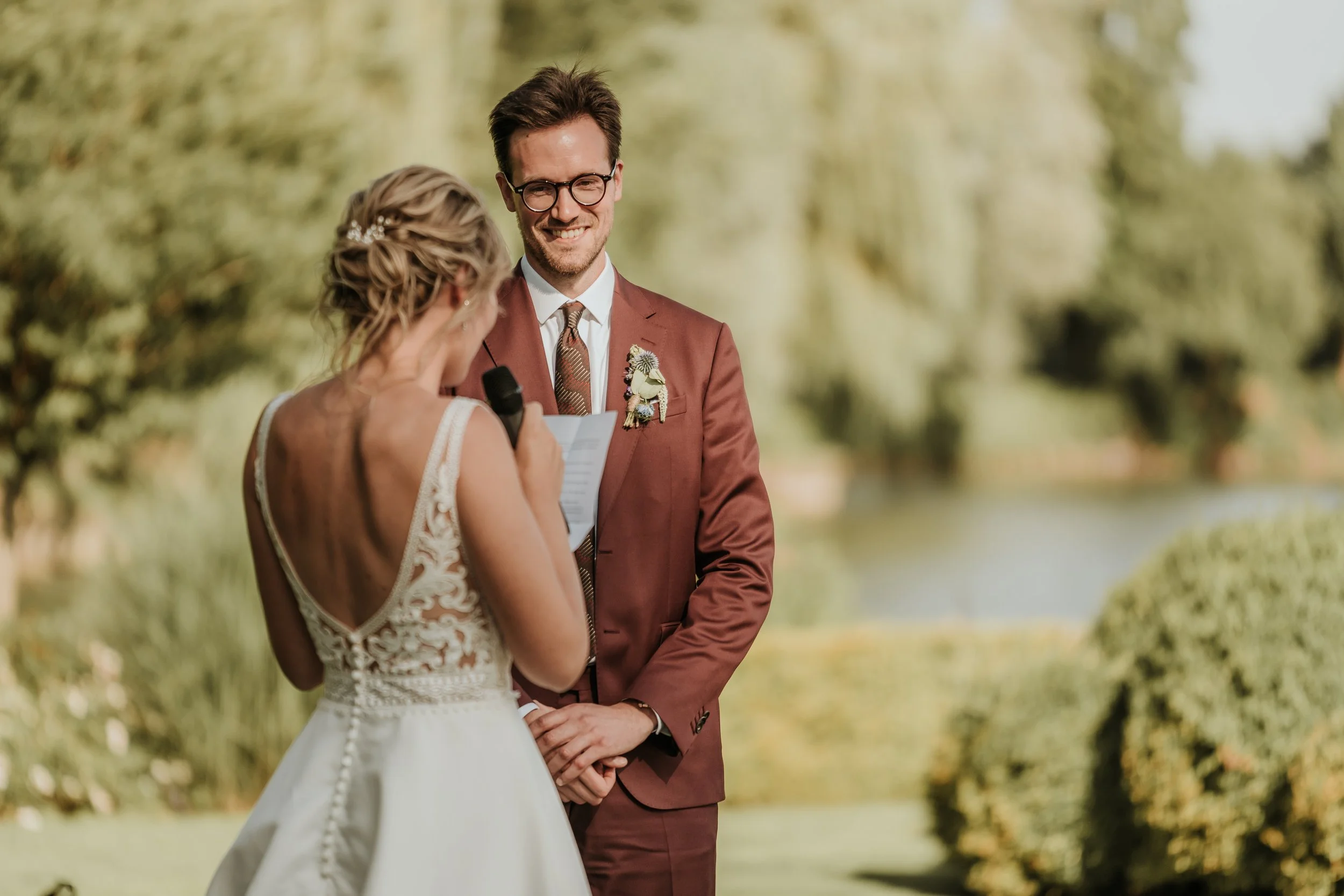Bruidegom en bruid tijdens het huwelijksceremonie buiten, met de bruid die de geloften leest.