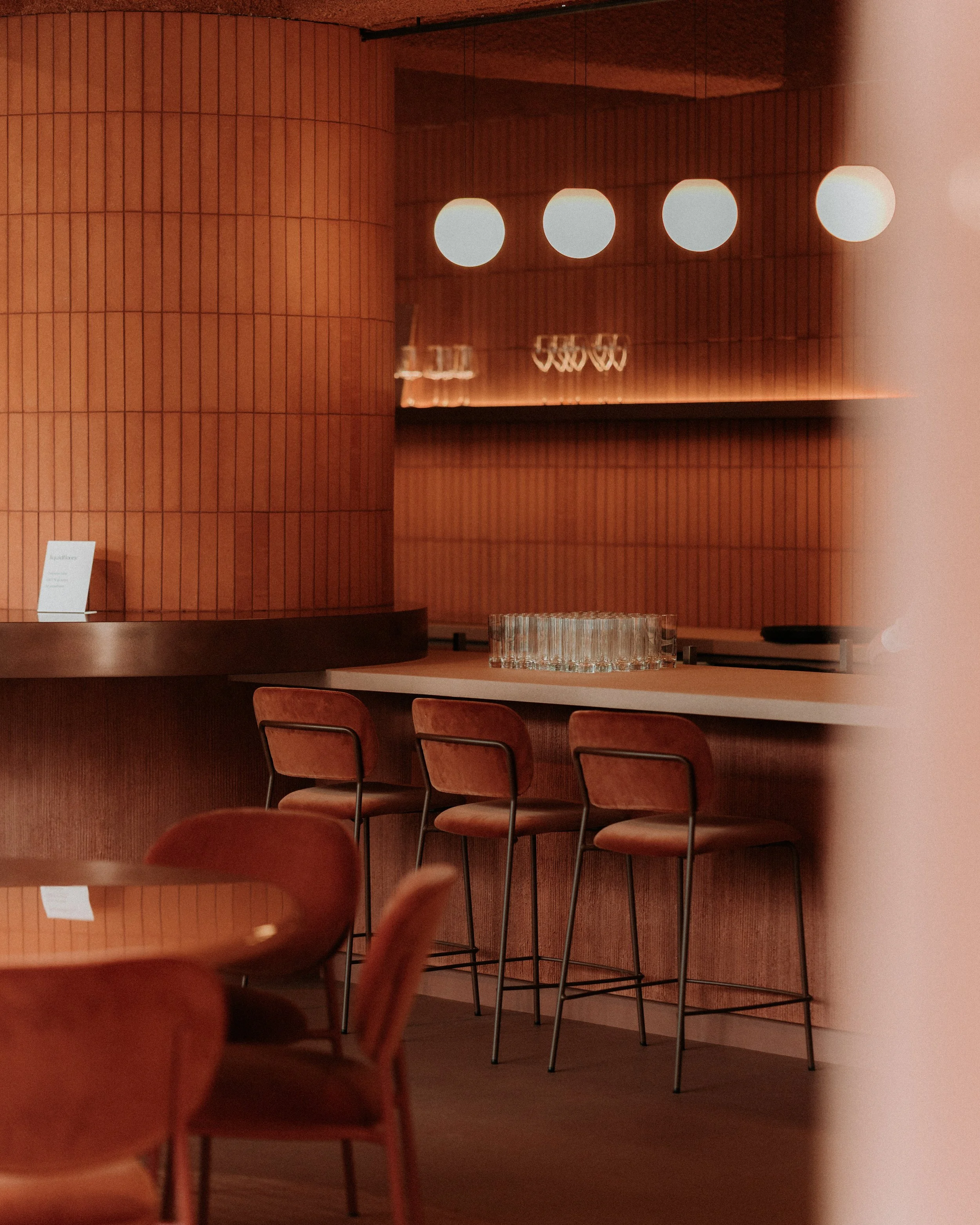 Een moderne bar met houten wanden en een overloop aan barkrukken onder warm licht.