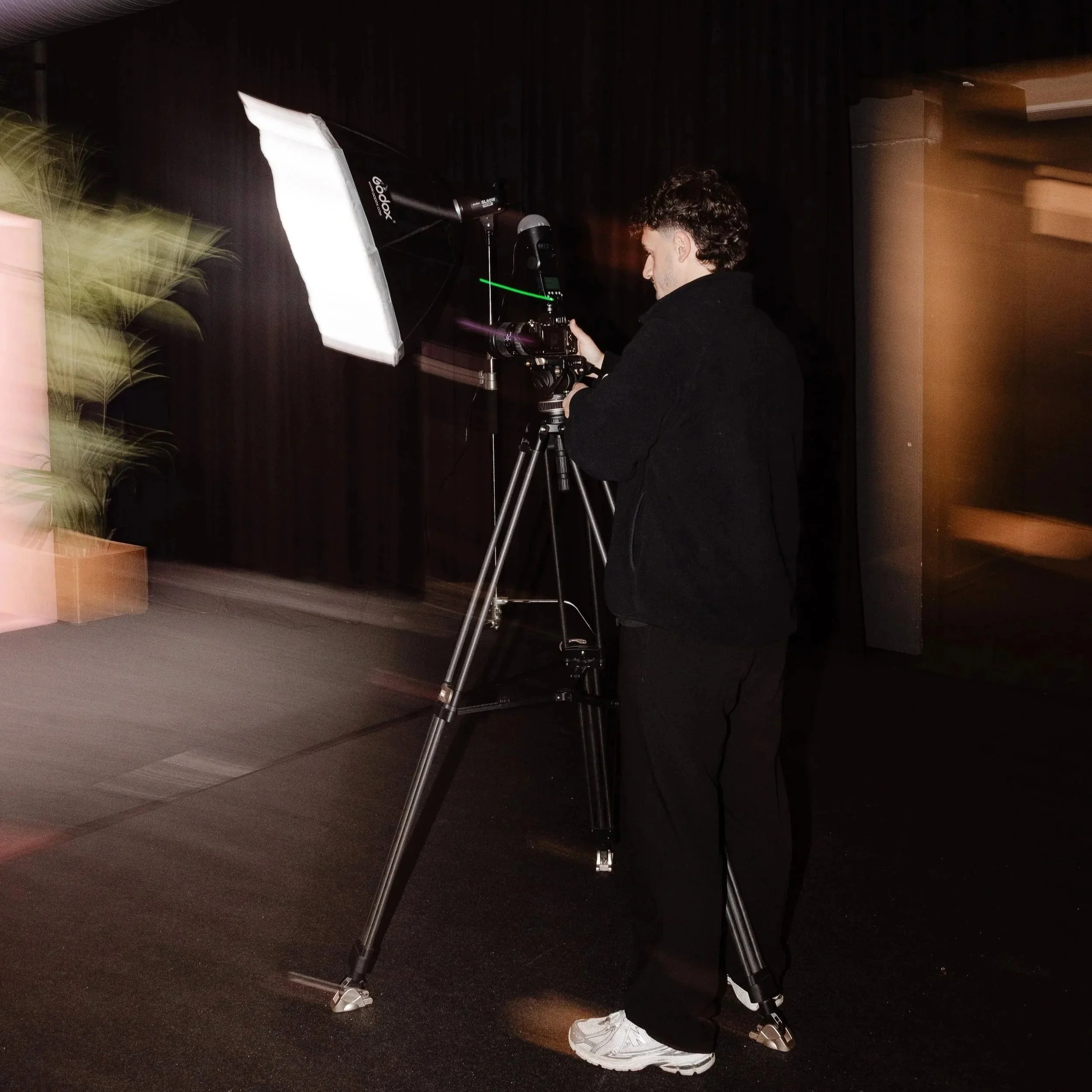 Een persoon die foto's maakt met een professionele camera op een statief in een donkere ruimte met bewegingsvlekken.