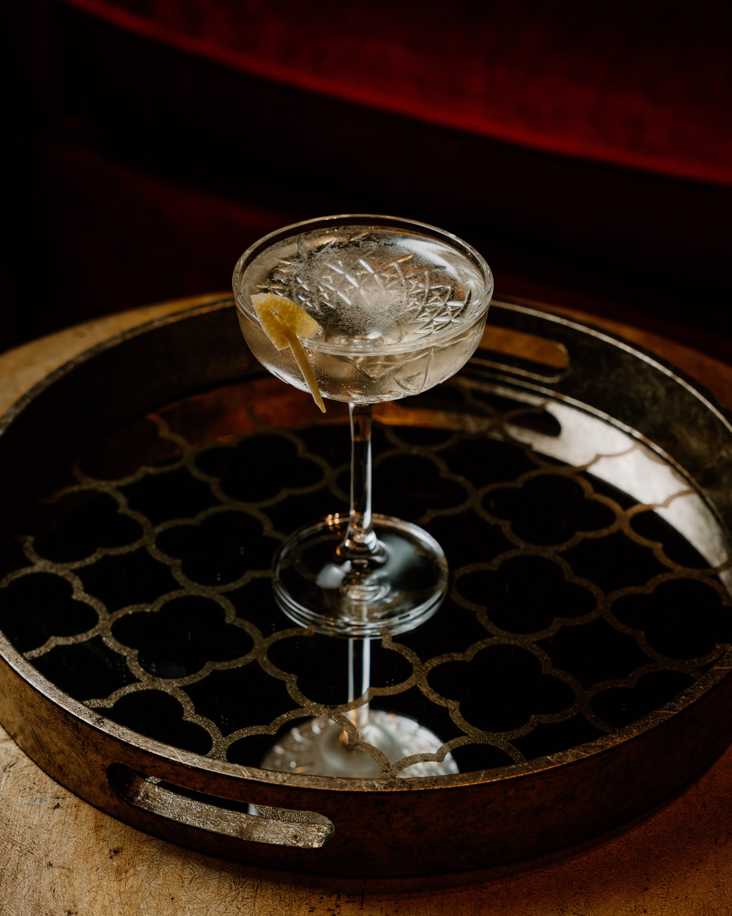 Een cocktailglas met een drankje en een citroenschijfje op een houten dienblad.