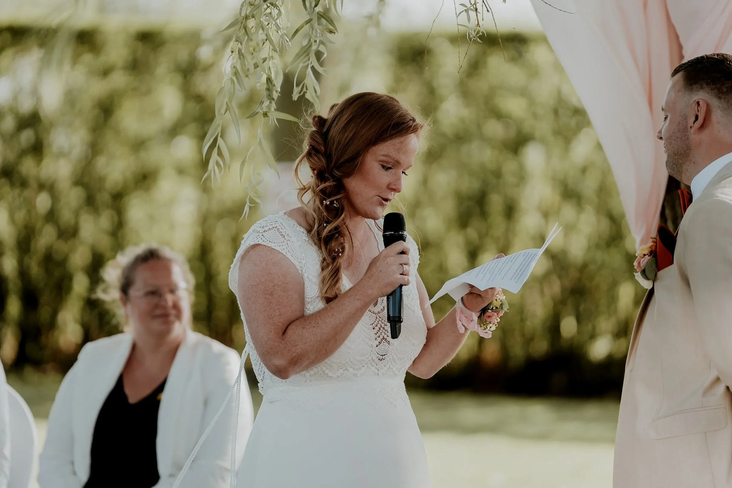 Vrouw leest een geloften en houdt een microfoon tijdens een buitenbruiloft.