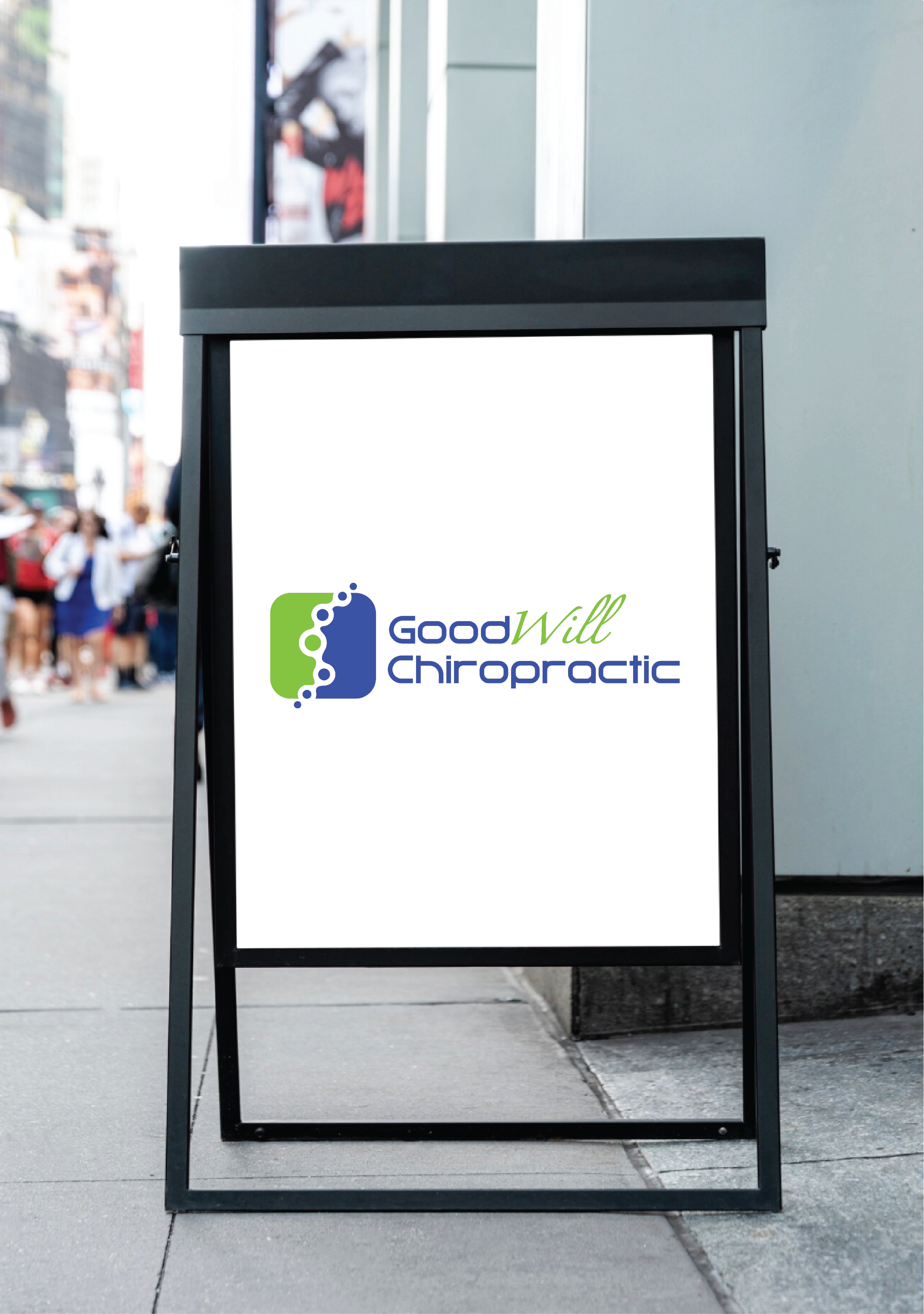 Street sidewalk with a black A-frame sidewalk sign displaying the logo for Good Will Chiropractic, consisting of a blue and green icon with text.
