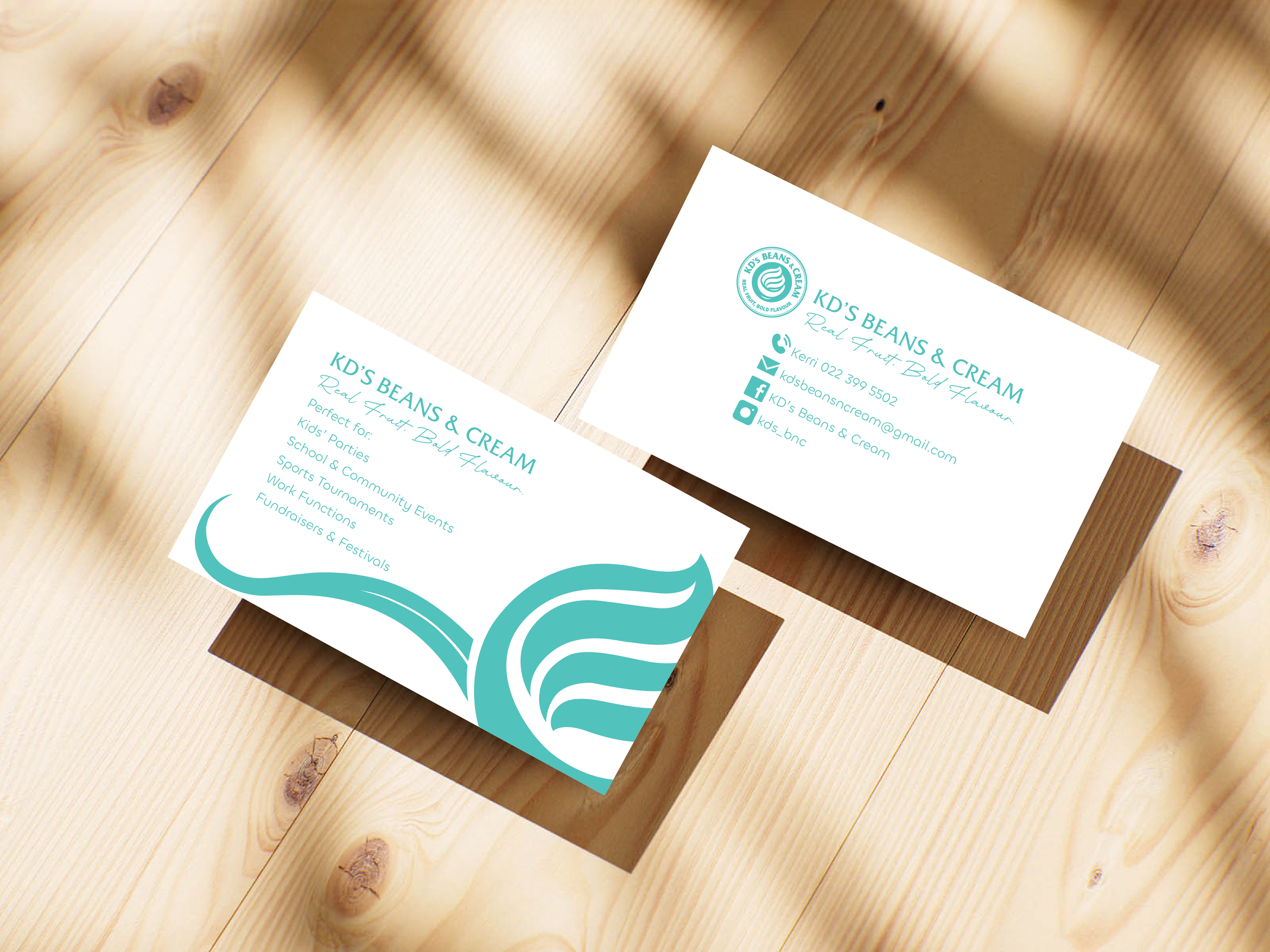 Two business cards for KD's Beans & Cream on a wooden surface, one showing contact details and the other displaying services including kids' parties, school and community events, and fundraisers, with a teal and white logo featuring a stylized coffee bean and waves.