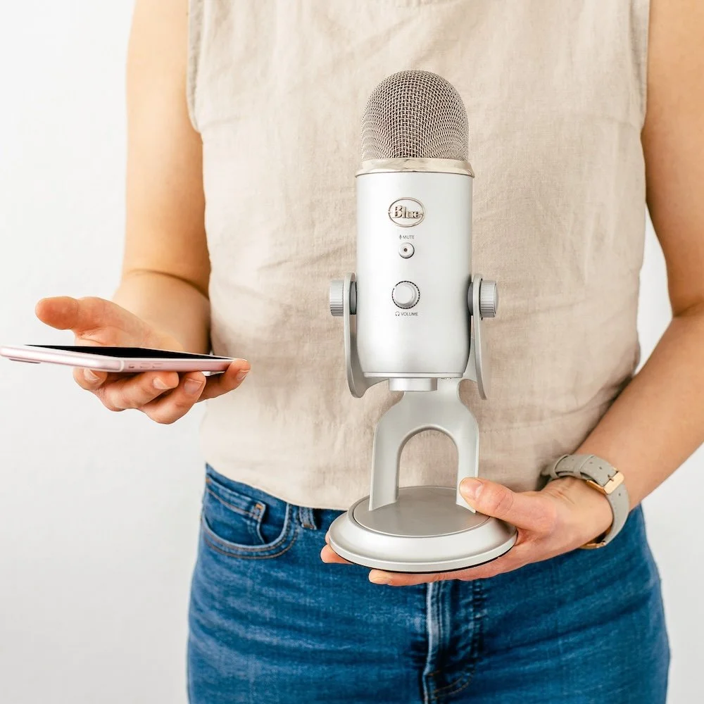 Person holding a smartphone in one hand and a silver microphone on a stand in the other.