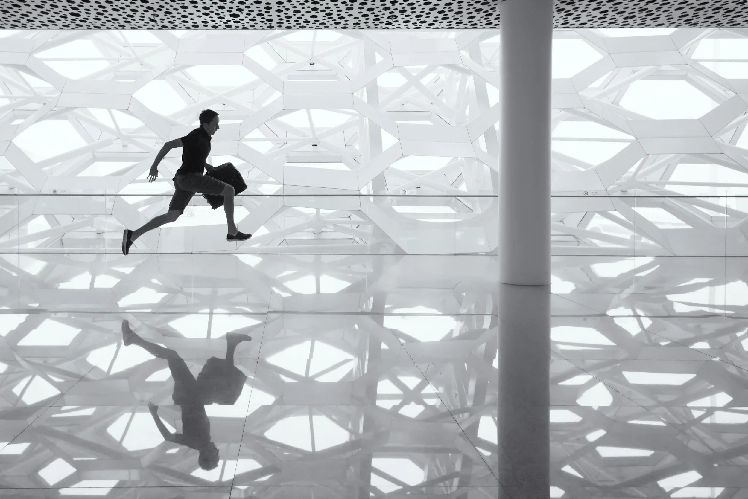 A man running in an airport or modern building with geometric white architectural design and reflective floor.