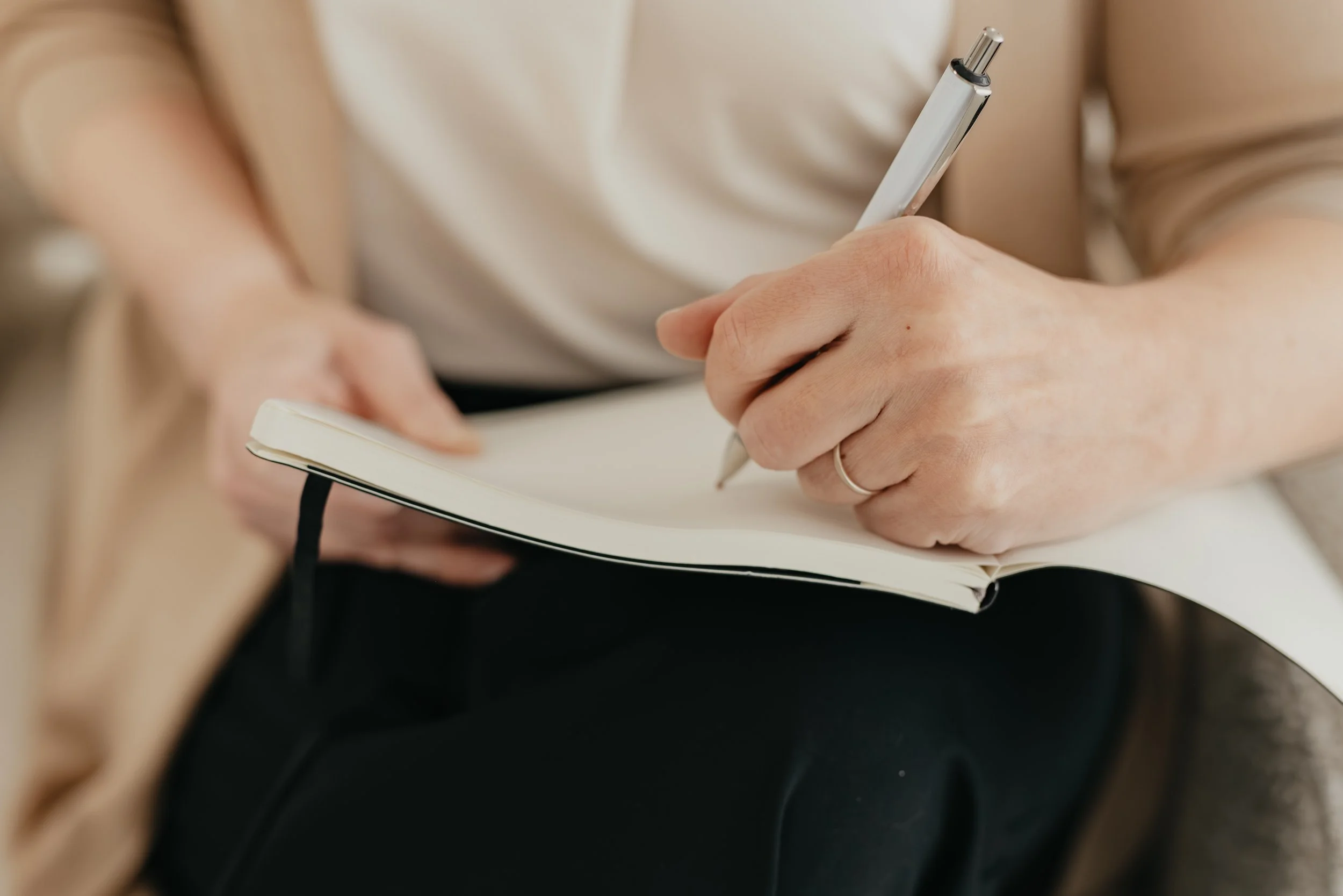 Close-up of a person holding a pen and writing in a notebook.
