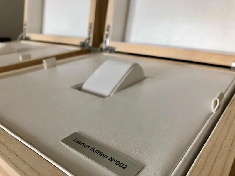 A wooden display case with a labeled item reading 'Launch Edition N0002' inside, featuring a white, curved object.