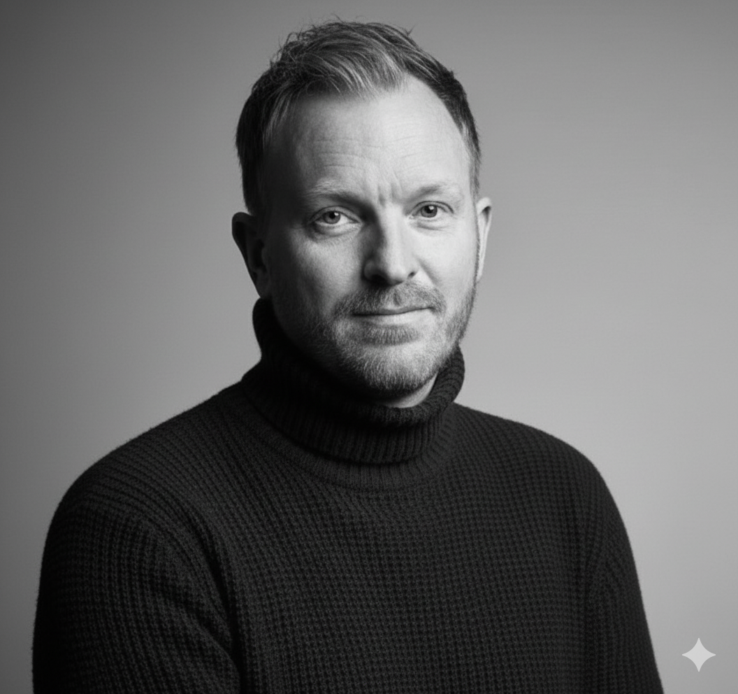Black and white portrait of a man with short hair, a beard, wearing a turtleneck sweater, looking at the camera with a neutral expression.