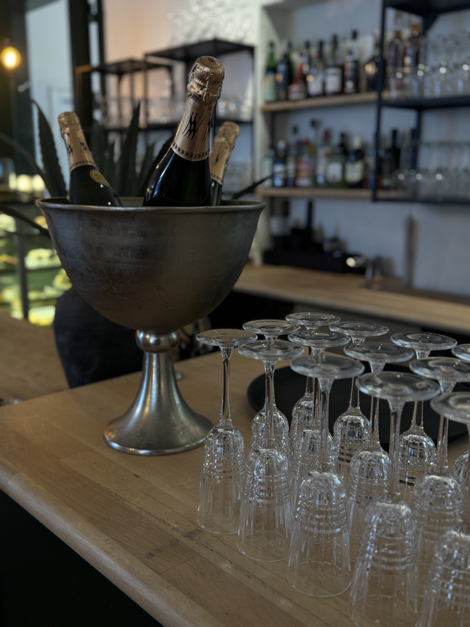 Champagneflasker i en sølvskål og tomme cocktailglas på en træbordplade i en bar.