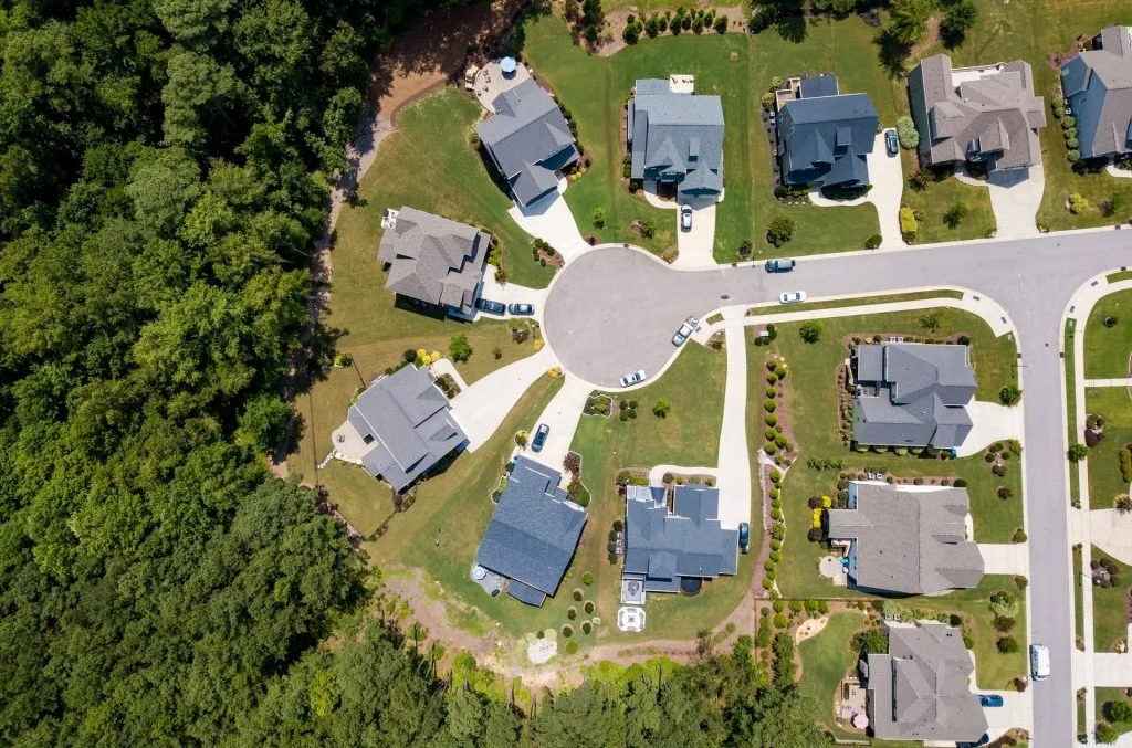 Aerial view of a suburban cul-de-sac with houses, manicured lawns, driveways, and surrounding trees.