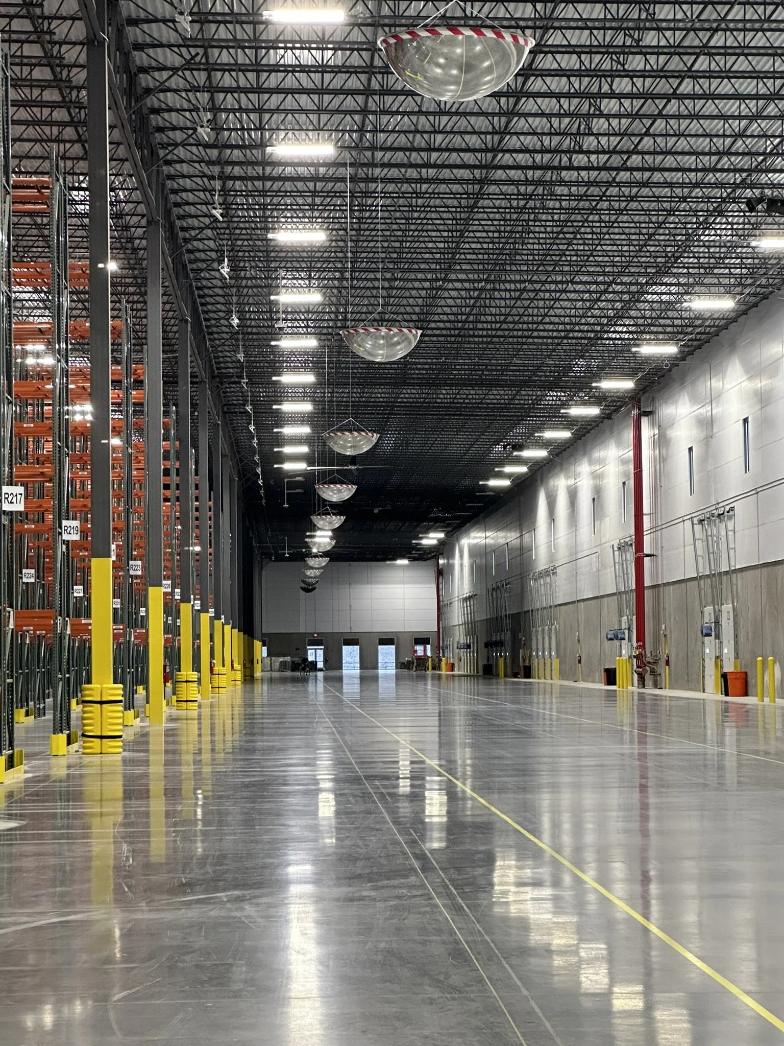 Spacious warehouse with high ceilings, LED lighting, and polished floors with safety lines. Features garage door access, ideal for office installations, equipment setup, warehouse cleaning, floor maintenance, and industrial facility services.