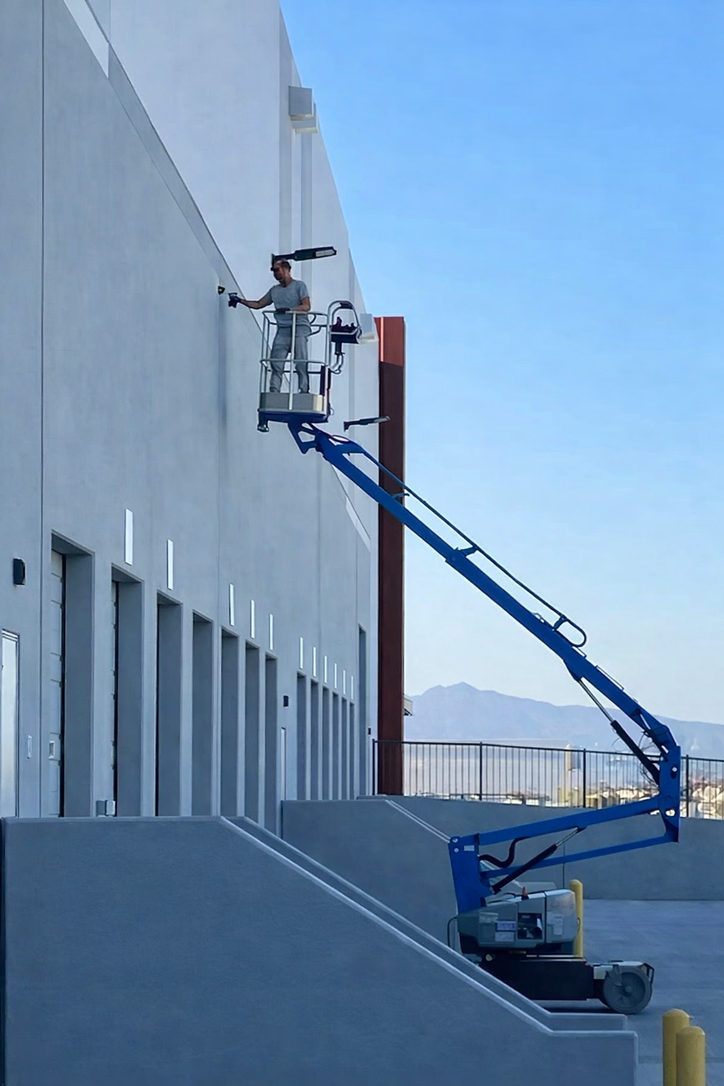A worker in a safety harness working on the exterior wall of a building from a hydraulic lift.