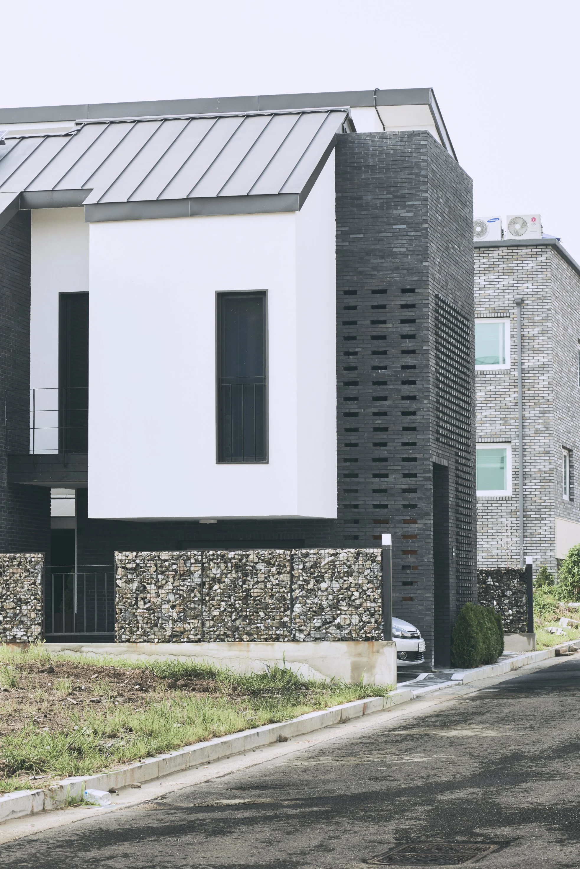 Modern house with black and white exterior, metal roof, small front yard, and a car parked inside the garage.