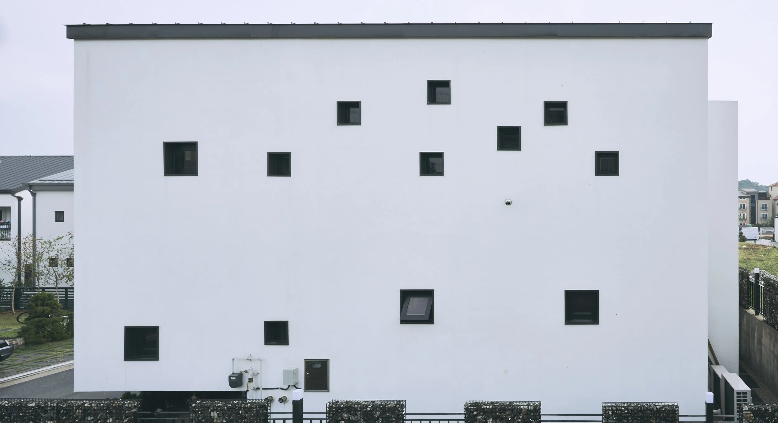 Modern white building with small square black windows scattered across the facade.