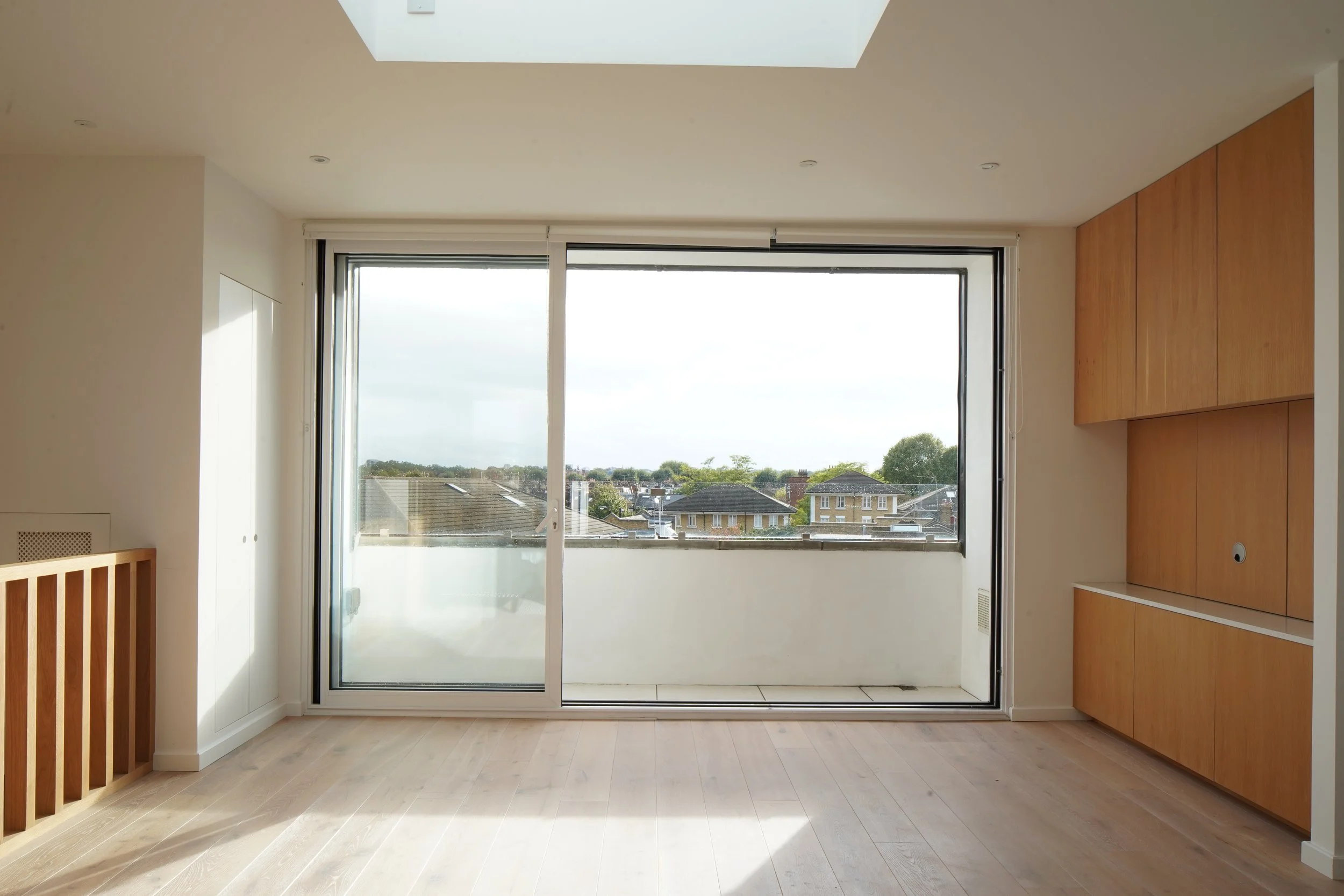 Empty living room with a large glass sliding door leading to a balcony, wooden cabinetry on the right, and light wood flooring.